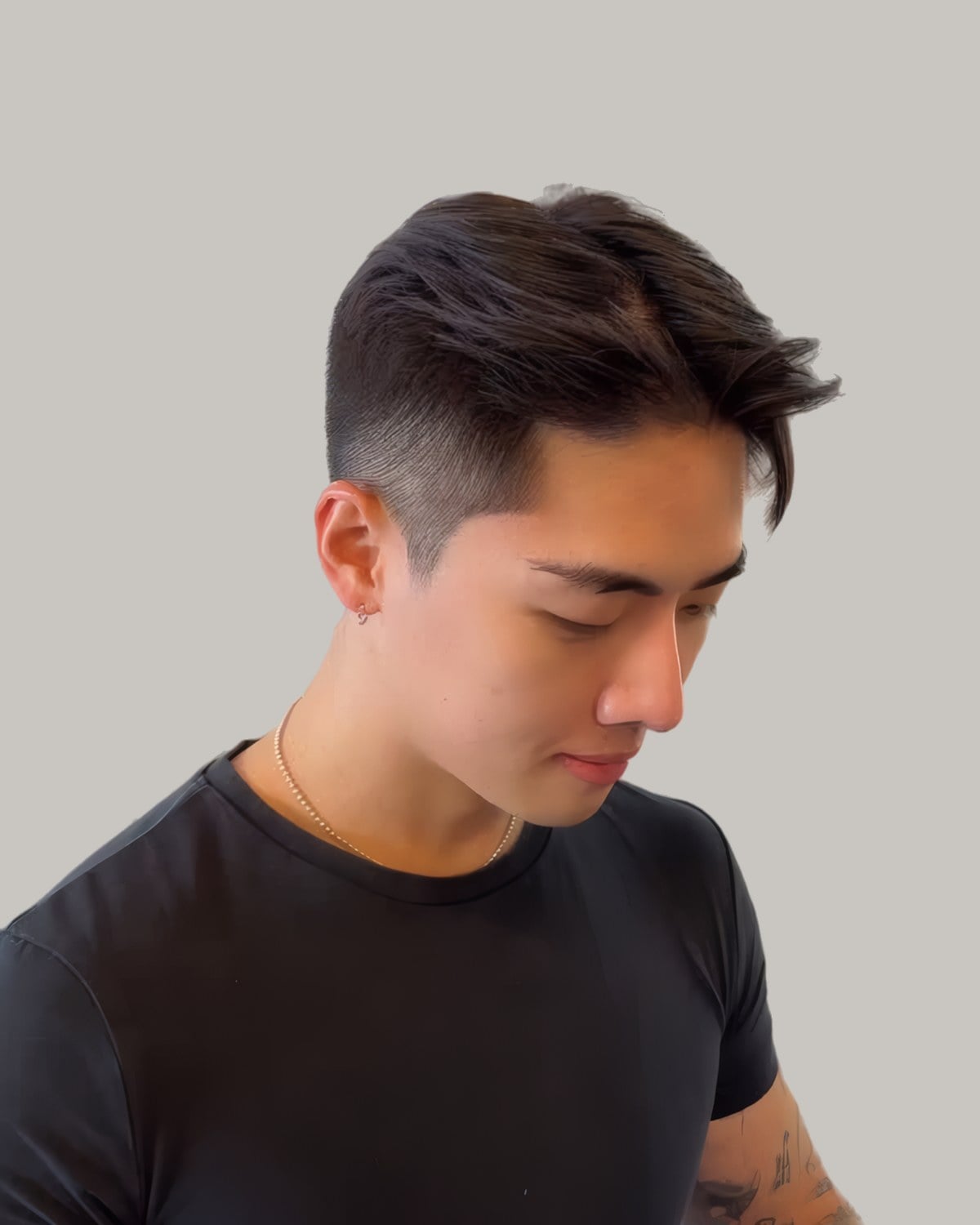 Young man in a black T-shirt with dark hair swept up and to the side over short sides, looking down