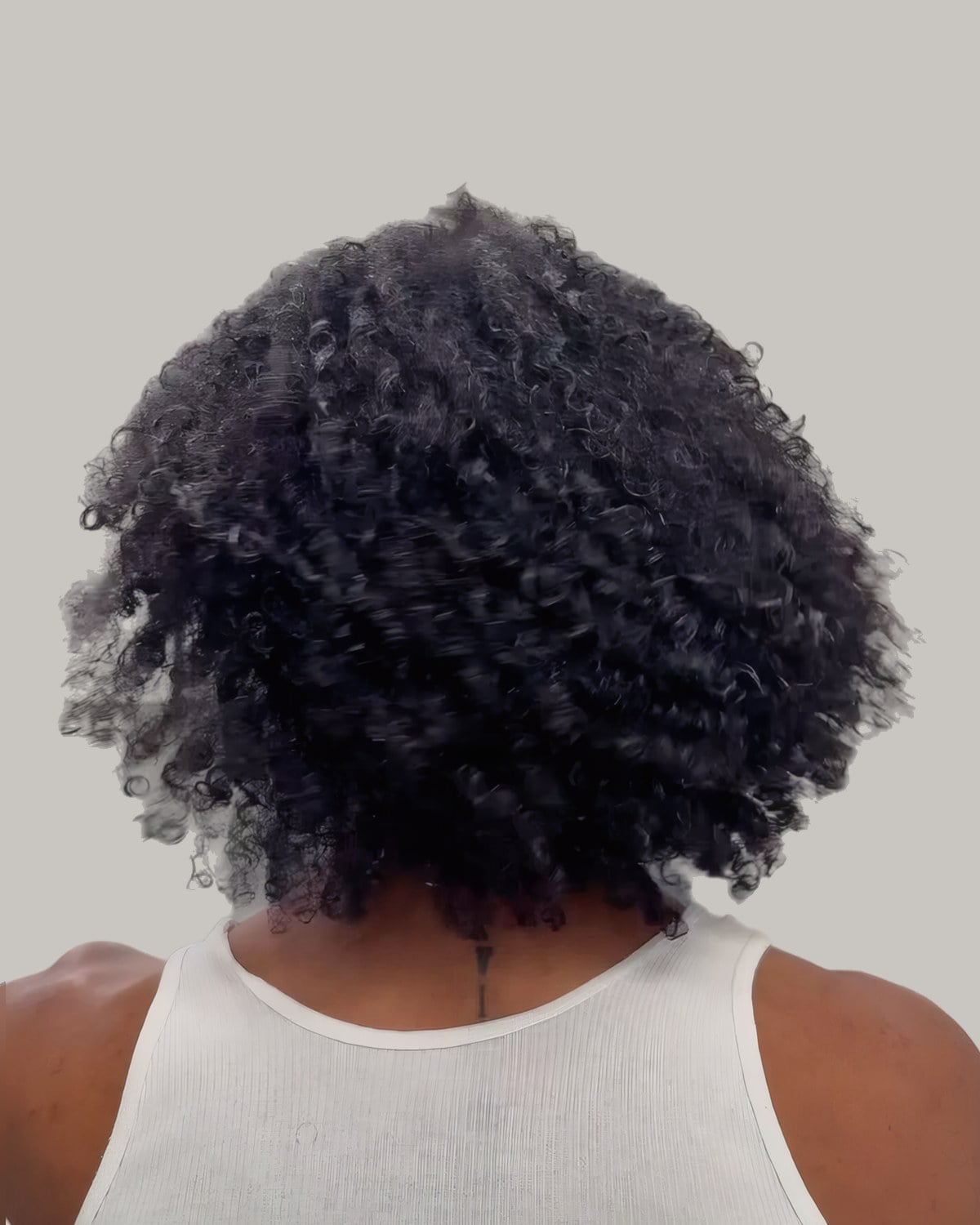 Man with a full, rounded afro, seen from behind in a white vest