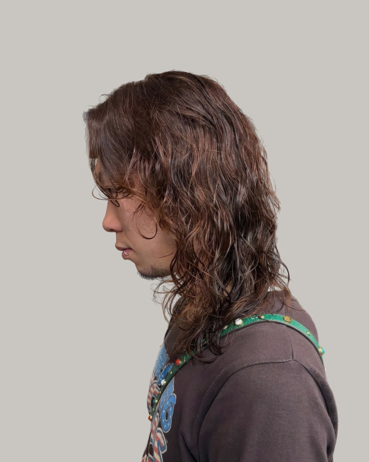 Man with long, layered brown waves falling past his shoulders, seen in profile