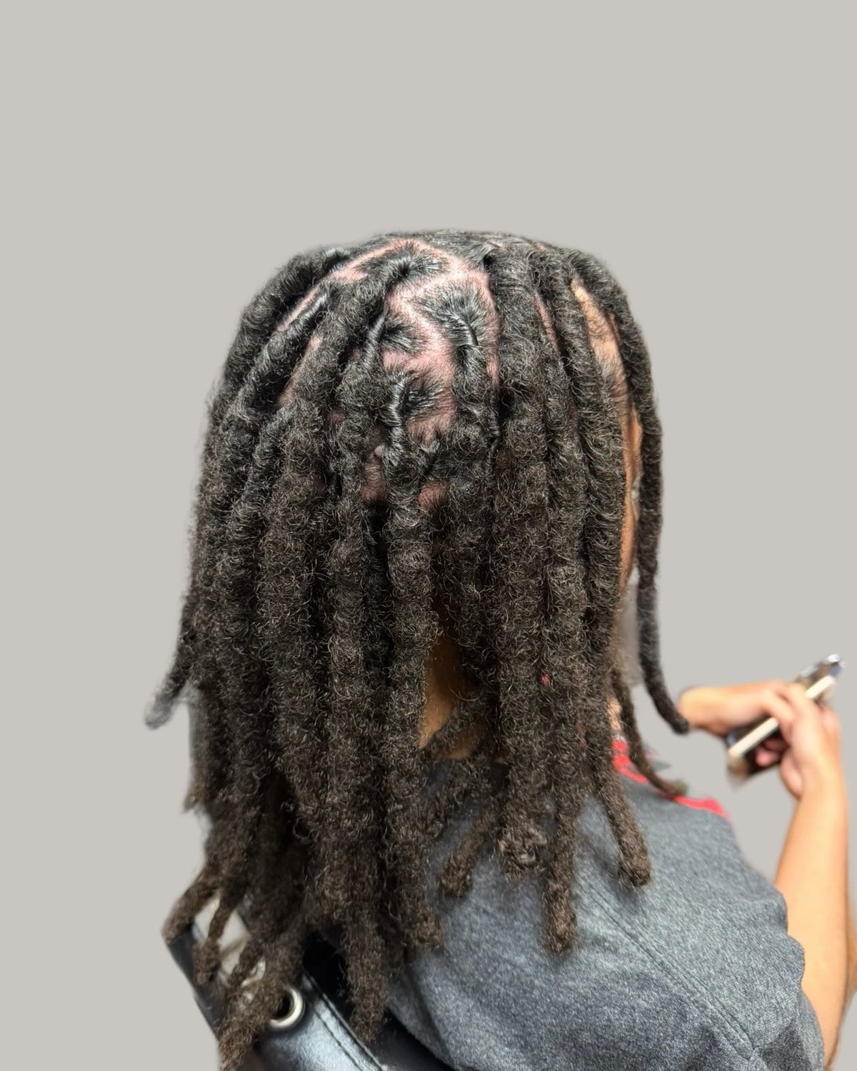 Man with long locs retwisted at the roots, seen from behind in a salon chair