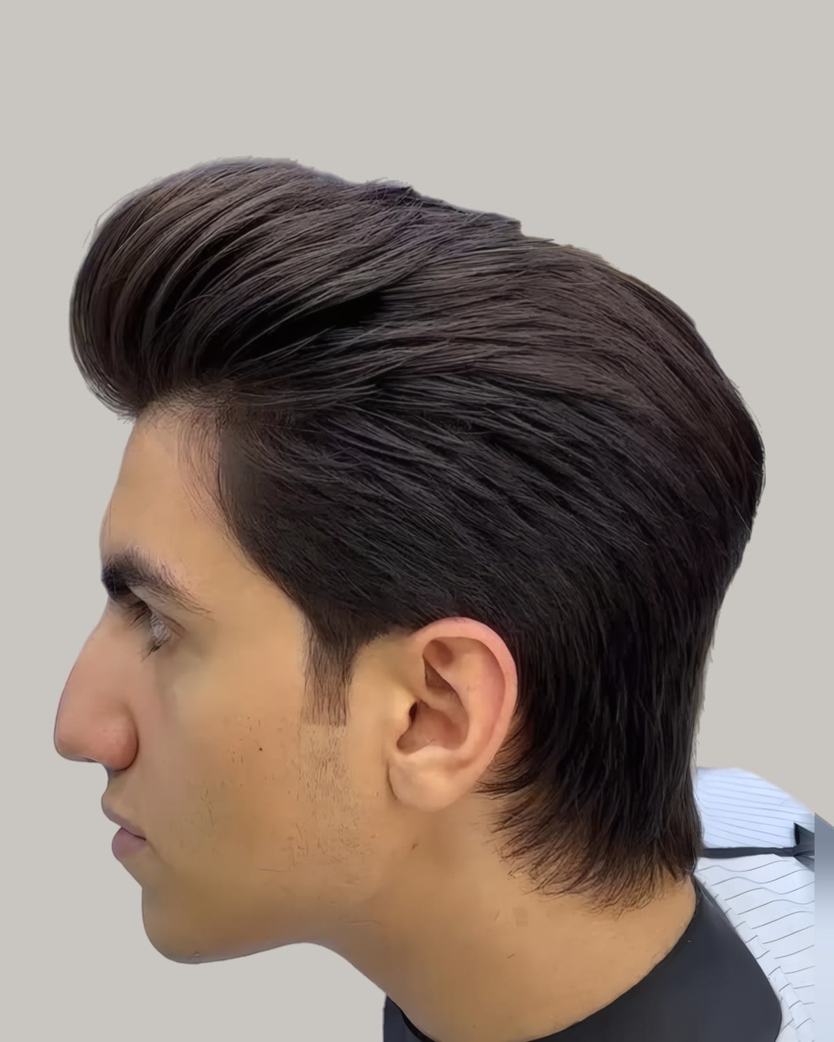 Man in a barber's cape with his hair swept up and back into a longer quiff, seen in profile