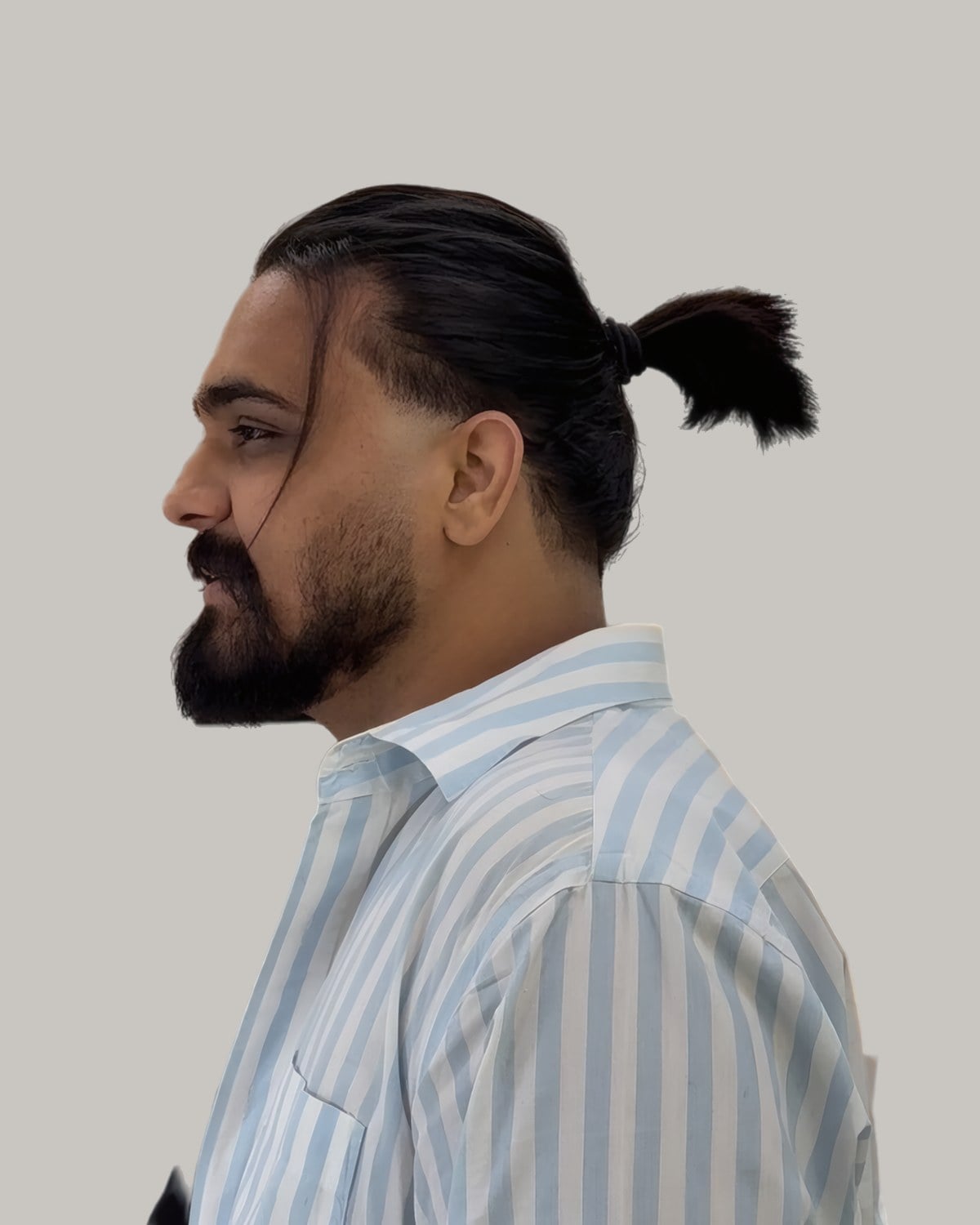 Bearded man in a striped shirt with his hair pulled back into a short, low ponytail, seen in profile
