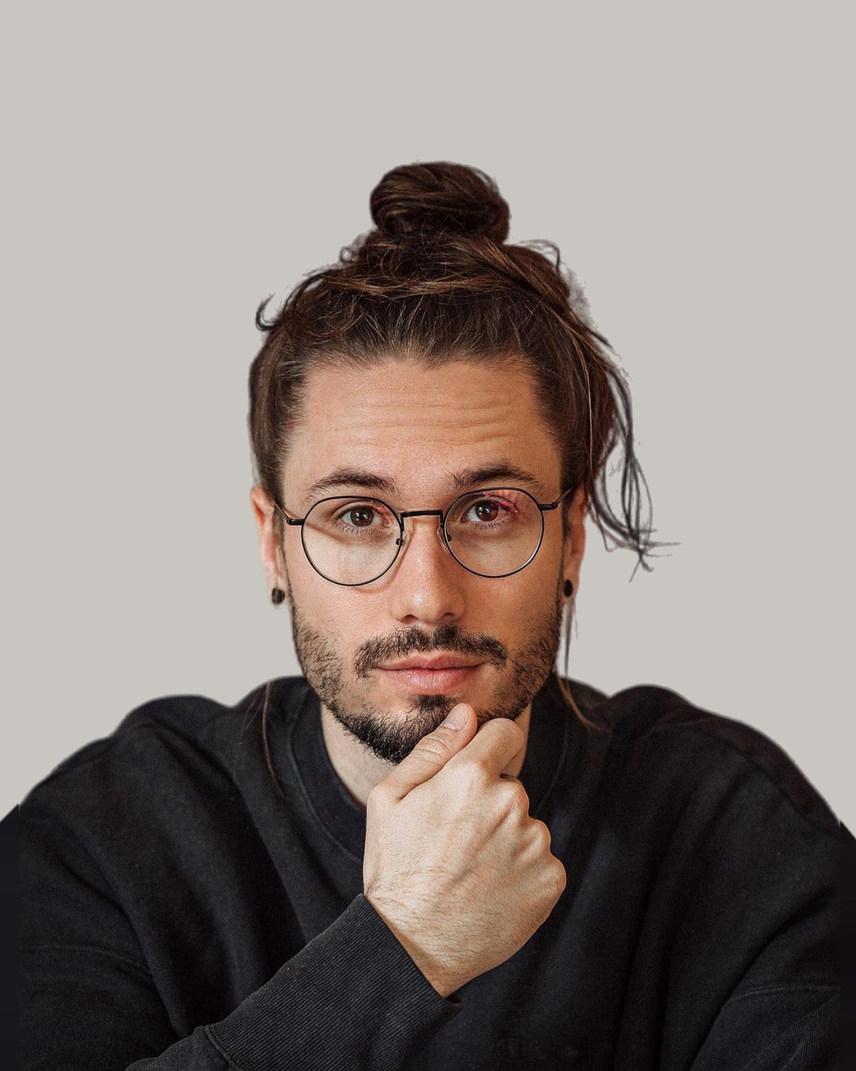 Man in round glasses with his hair tied in a bun on top of his head