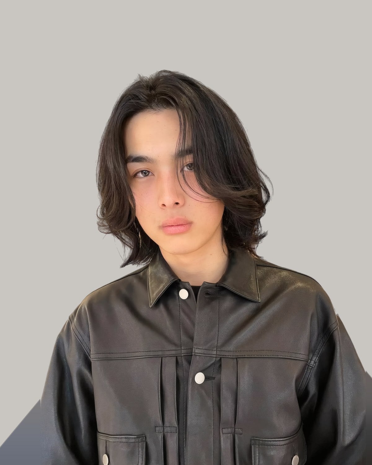 Young man in a leather jacket with dark hair parted in the middle and falling to his shoulders