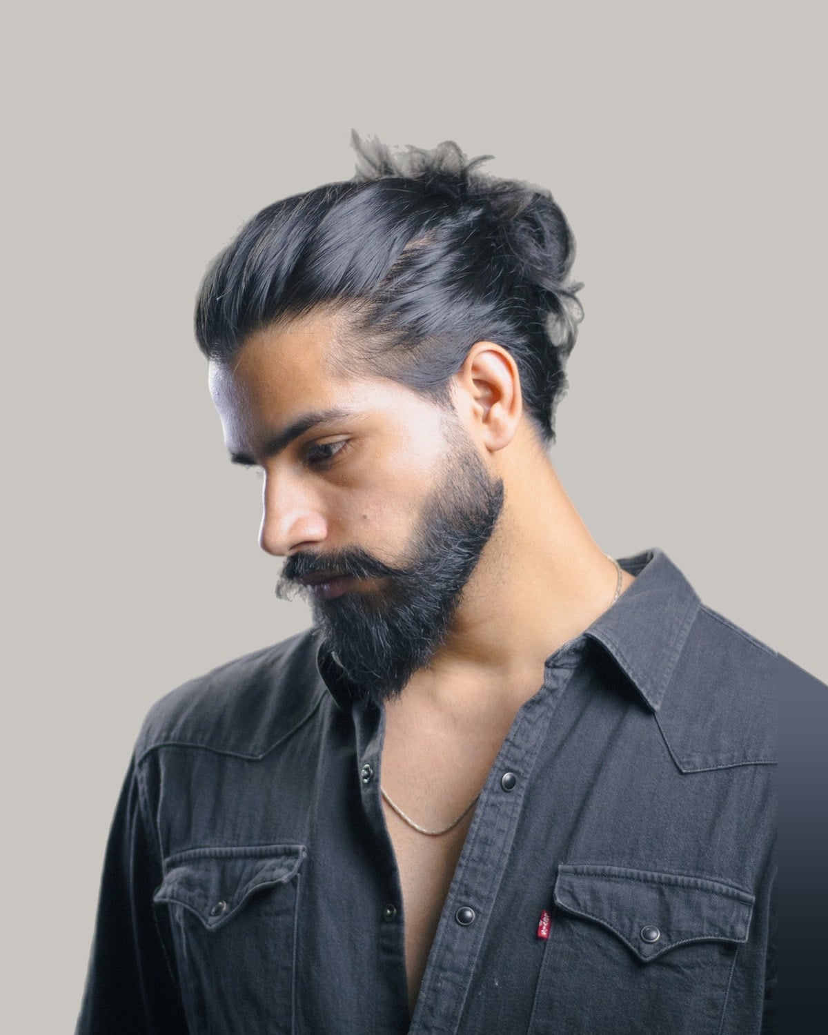 Bearded man with his long hair pulled back and tied high, looking down