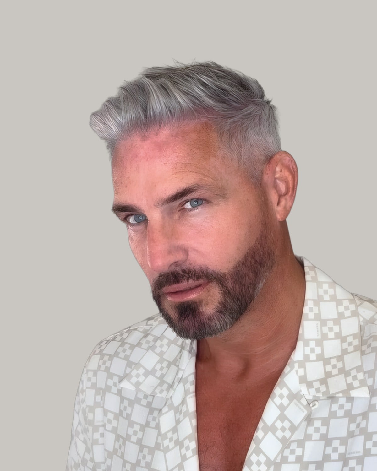 Grey-haired bearded man with his hair blow-dried up and back, in a patterned shirt