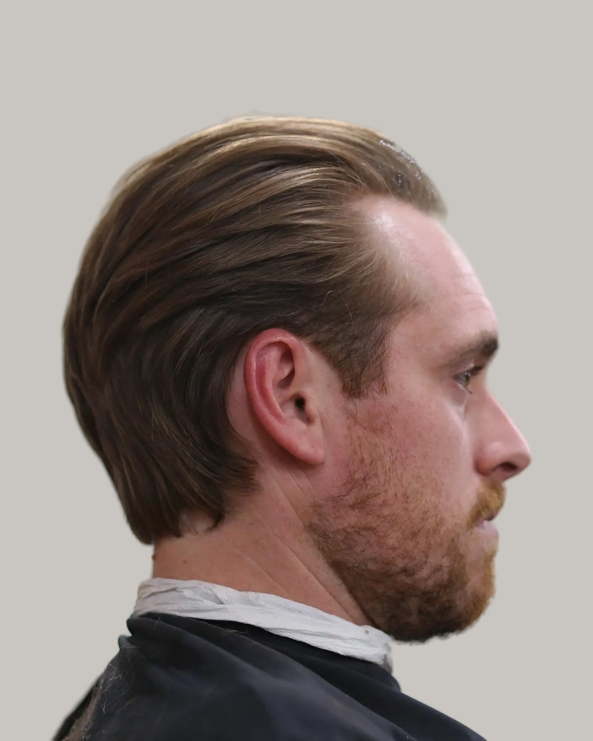 Man with a short ginger beard and light brown hair slicked back, seen in profile