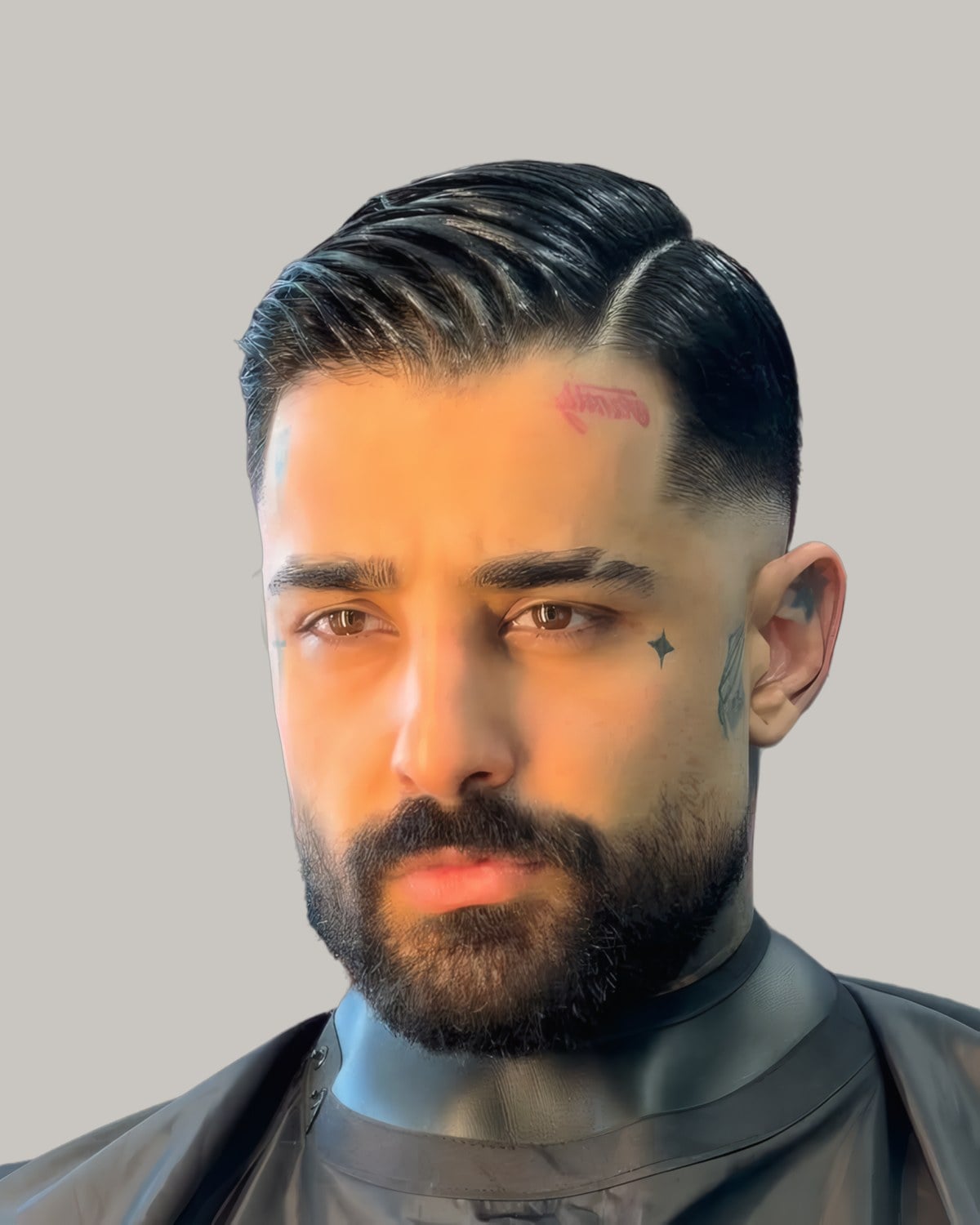 Bearded man in a barber's cape with dark hair combed from a sharp side part