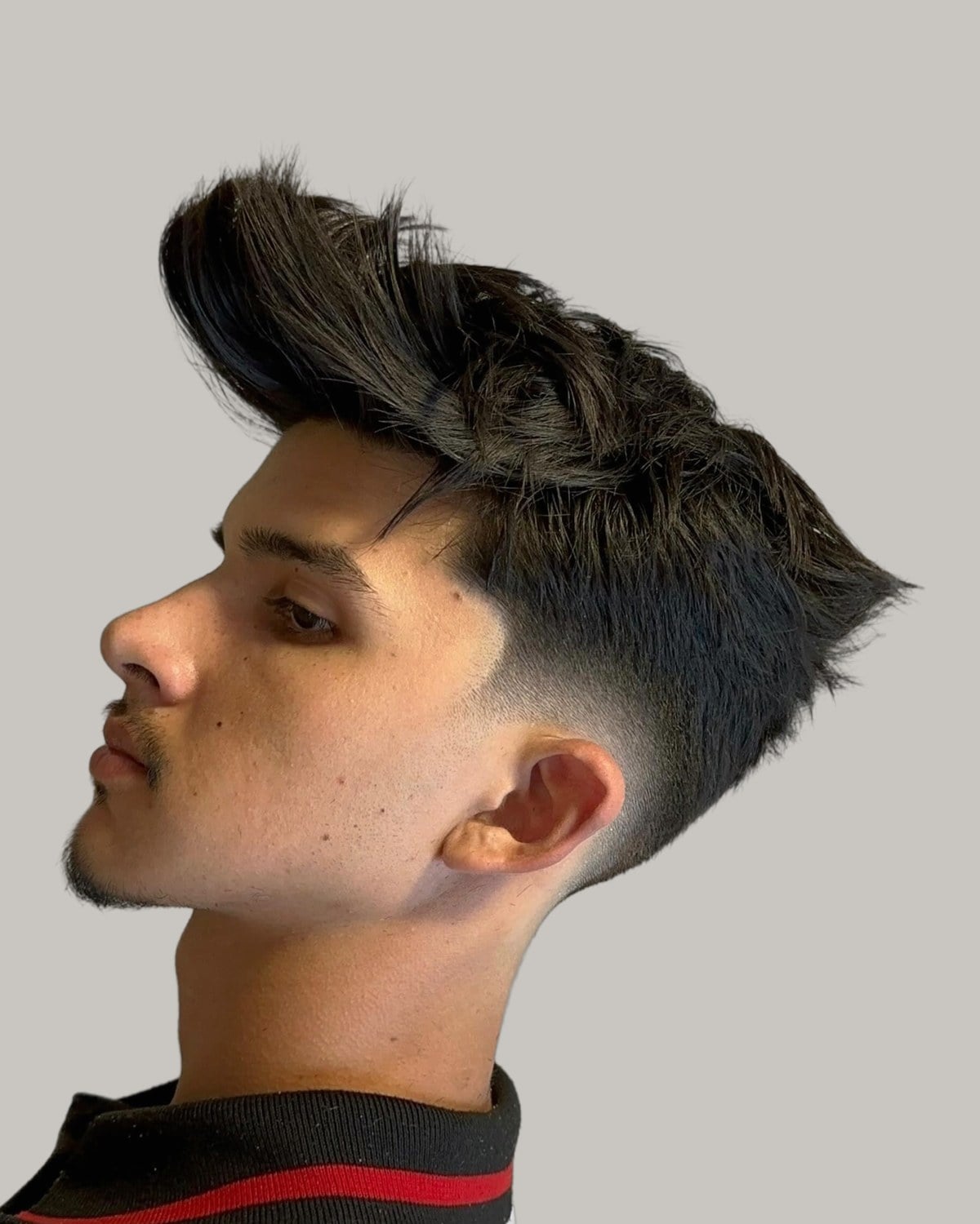Man with dark hair pushed up to a peak over faded sides, seen in profile