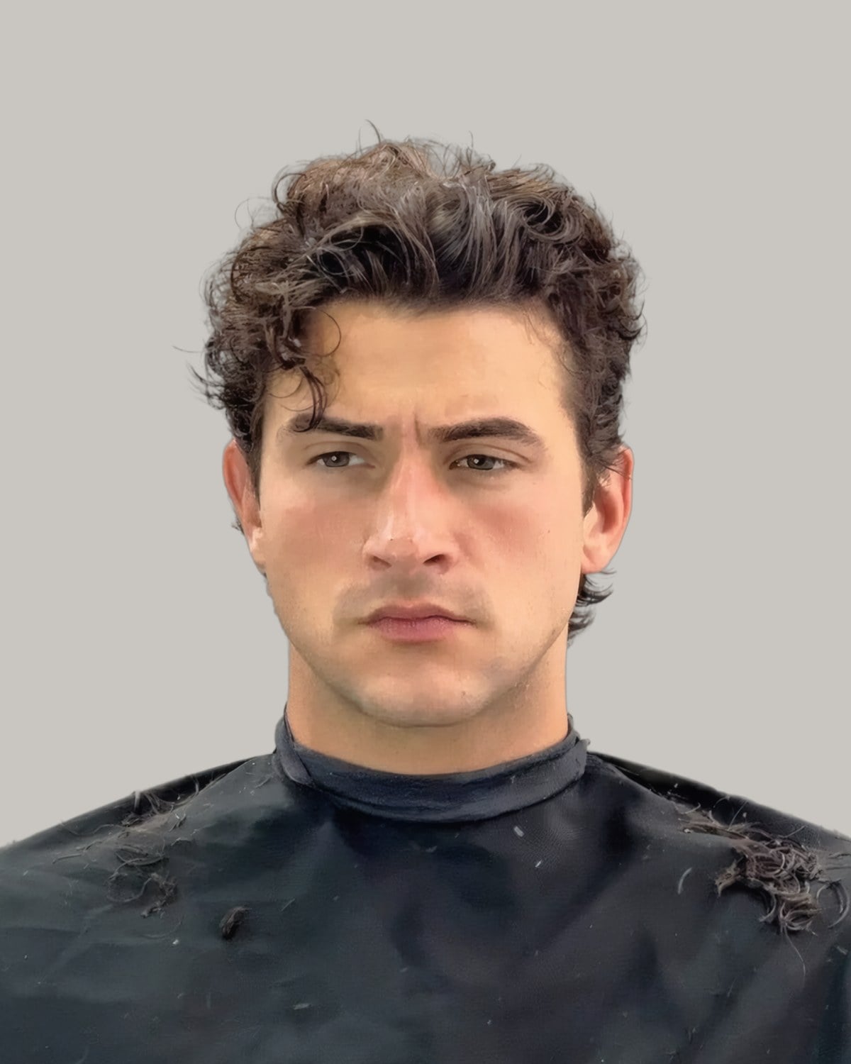 Man in a barber's cape with dark curls on top and shorter sides