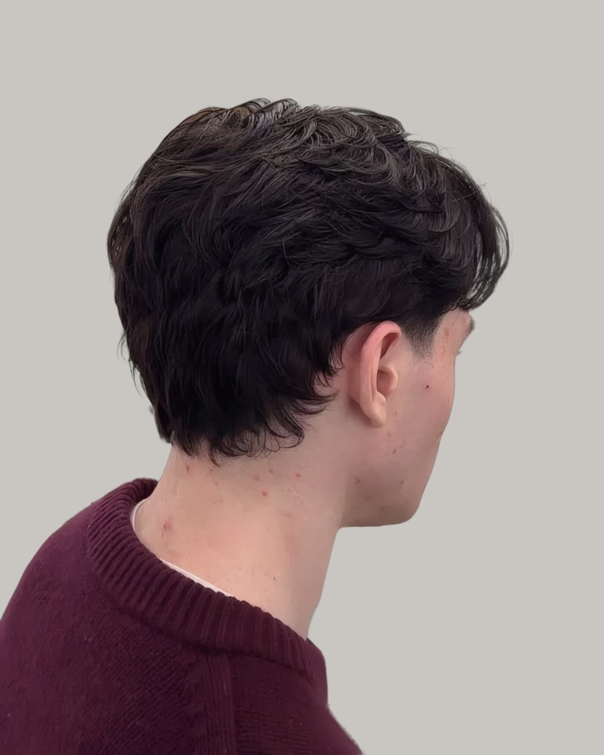 Man with dark wavy hair seen from behind at an angle, tapered at the neck