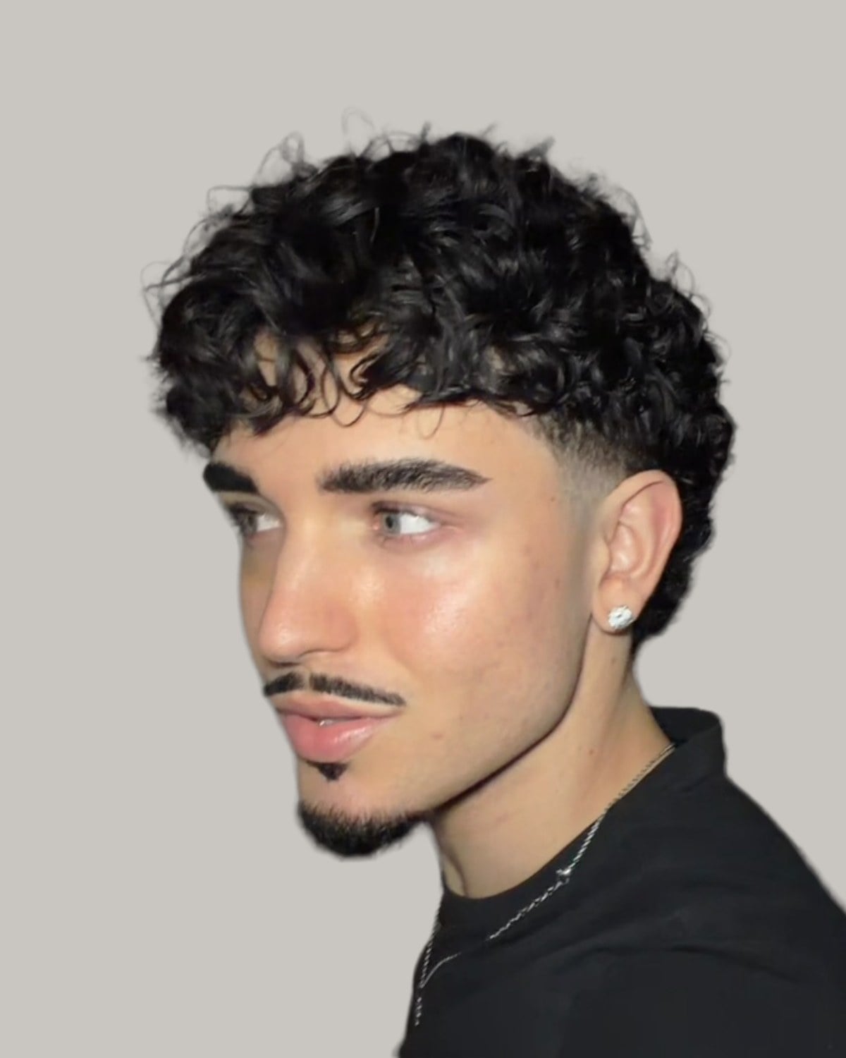 Man with a thin moustache and a curly mullet faded around the ear, looking to one side