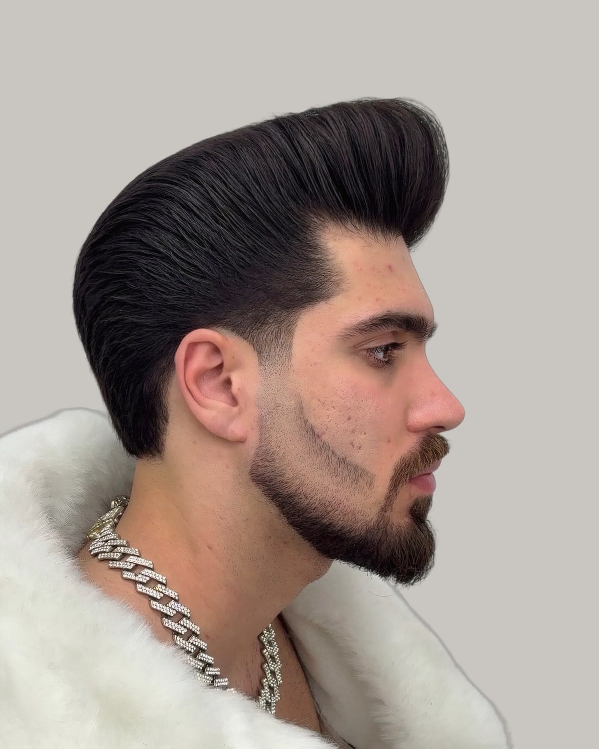 Bearded man with a tall dark pompadour and faded sides, seen in profile