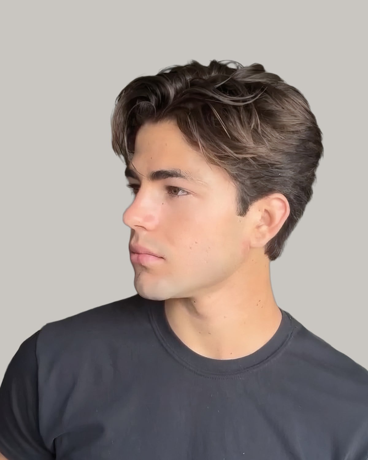 Young man with dark brown hair swept back from a side part, seen in three-quarter profile, in a grey T-shirt