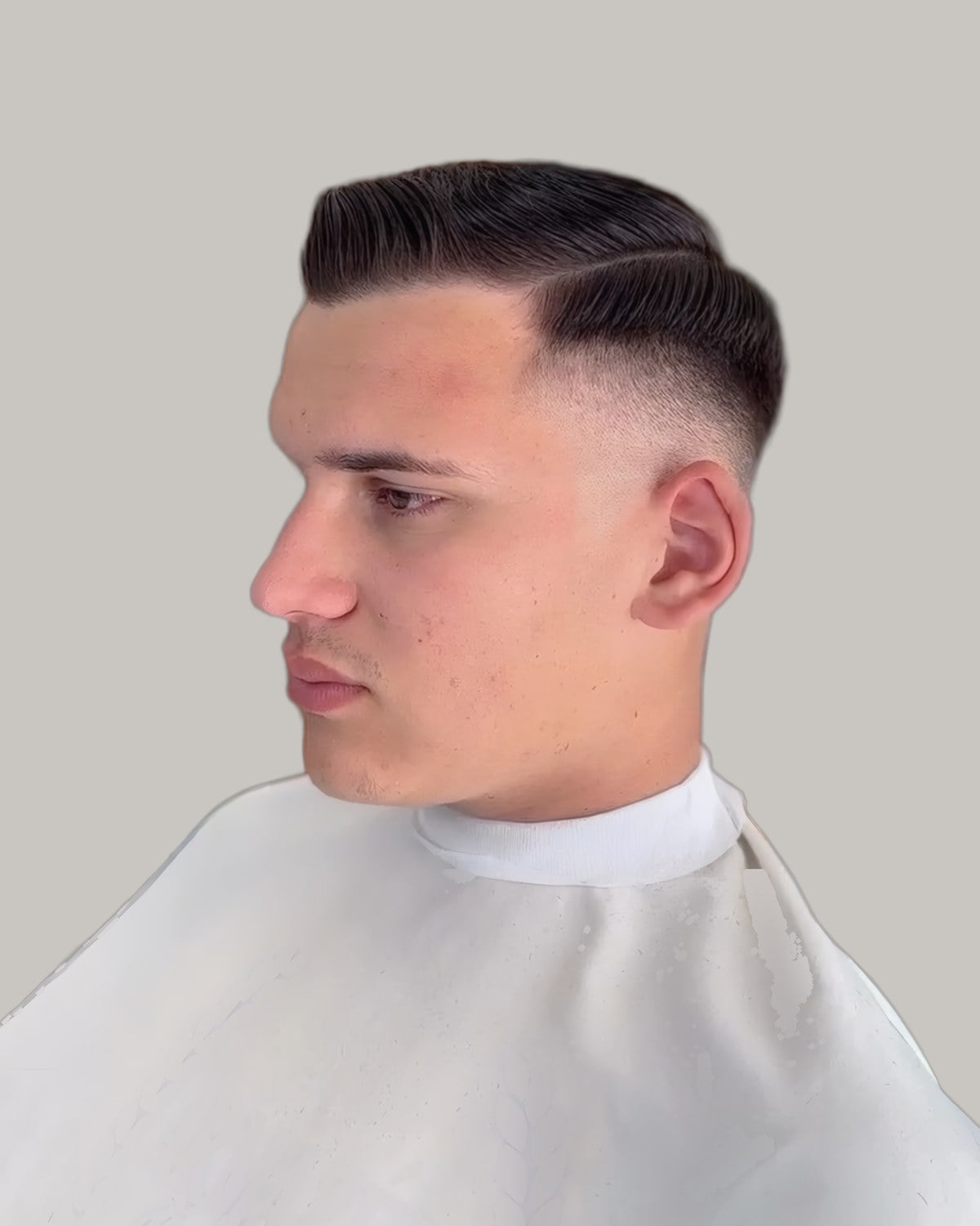 Man in a barber's cape with dark hair combed to the side over a skin fade