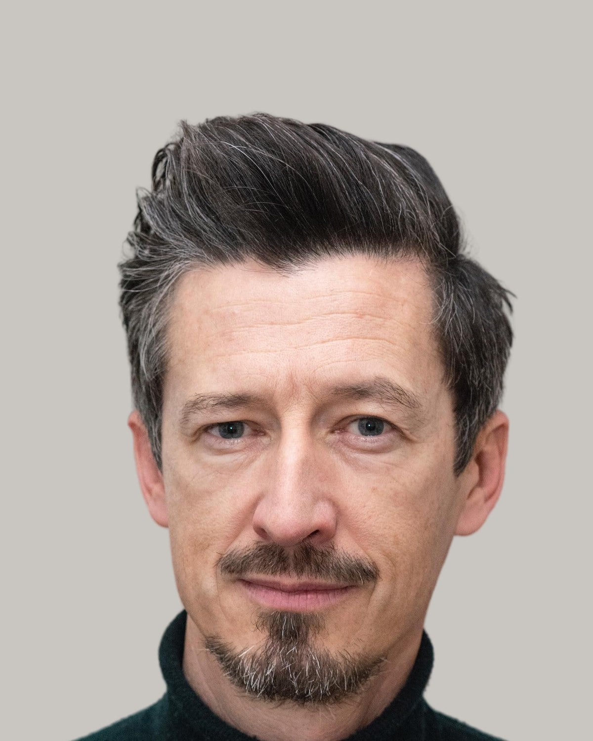 Man with dark hair streaked with grey, swept up and back, and a goatee, in a dark green turtleneck