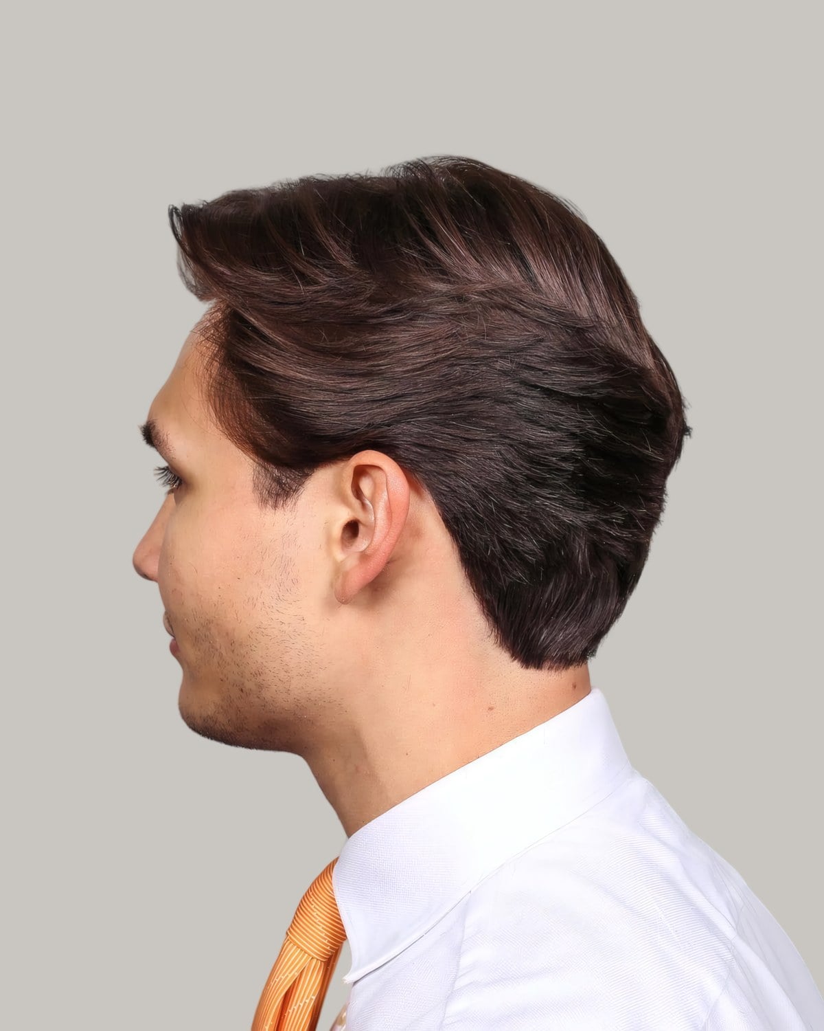 Man in a white shirt and an orange tie with dark brown hair swept up and back, seen in profile