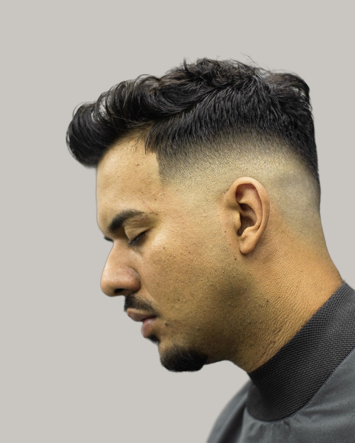 Bearded man with a dark quiff over a high skin fade, seen in profile