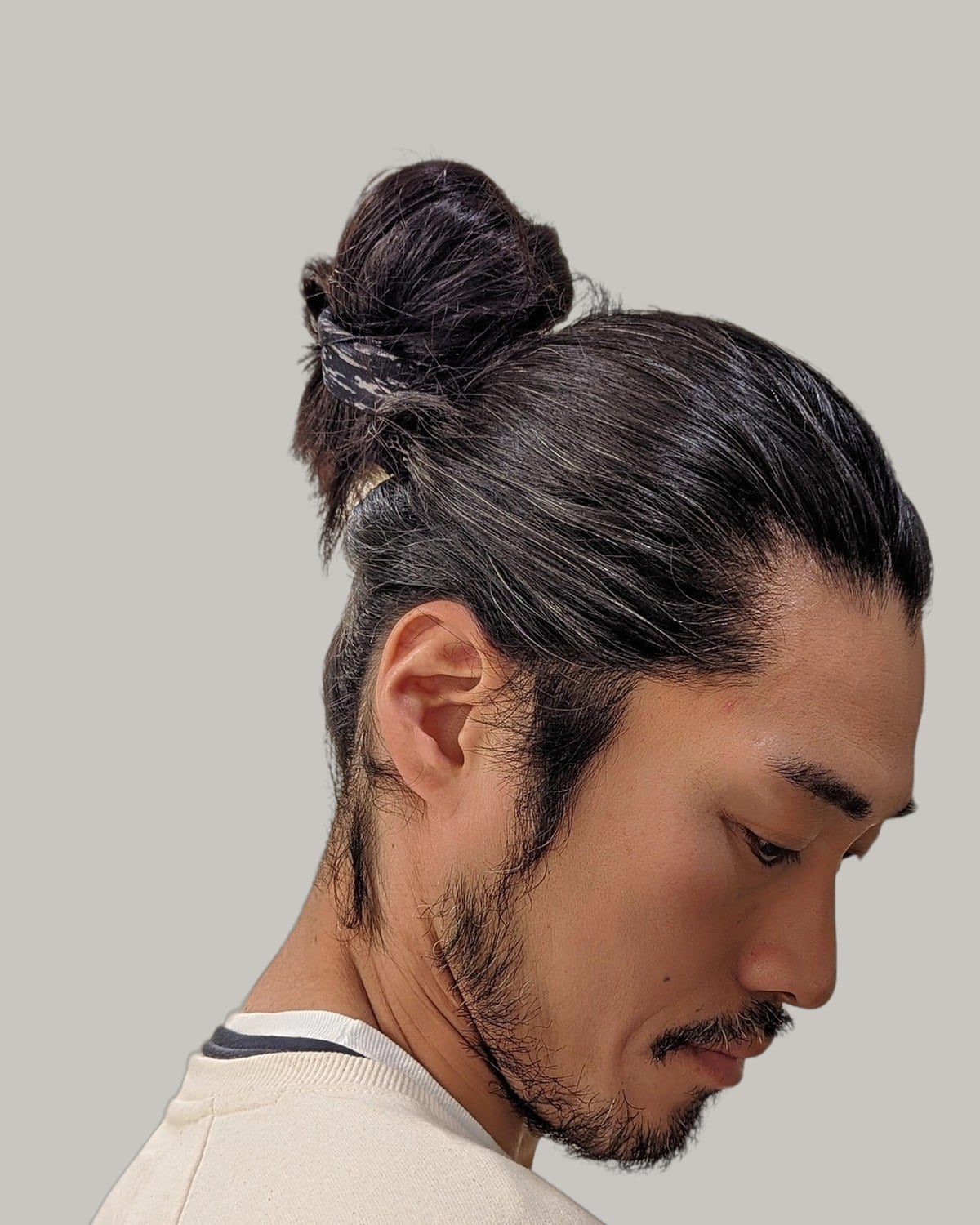 Bearded man with long dark hair tied up in a bun, loose strands at his face
