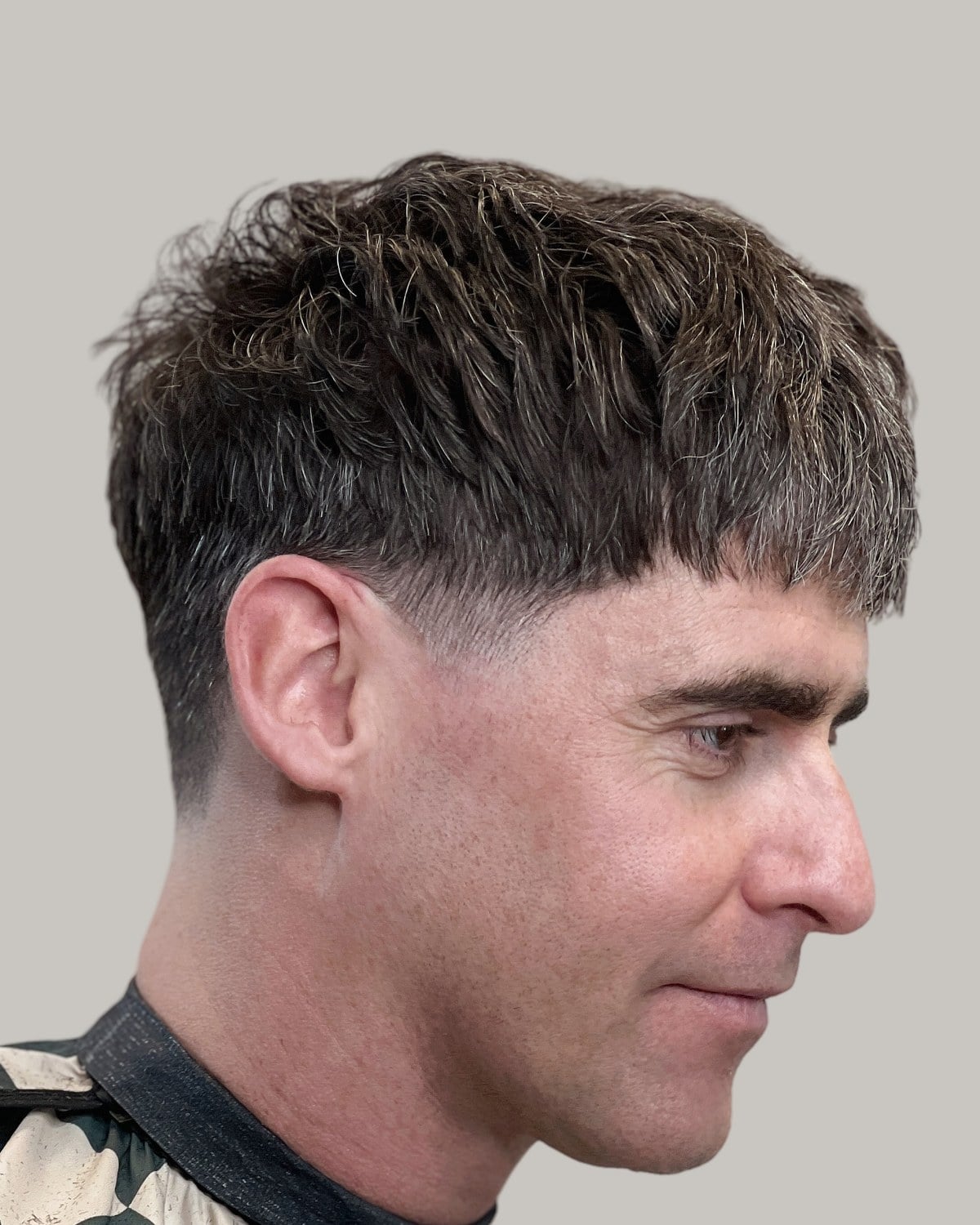 Man with a blunt Edgar fringe and a low taper, seen in profile