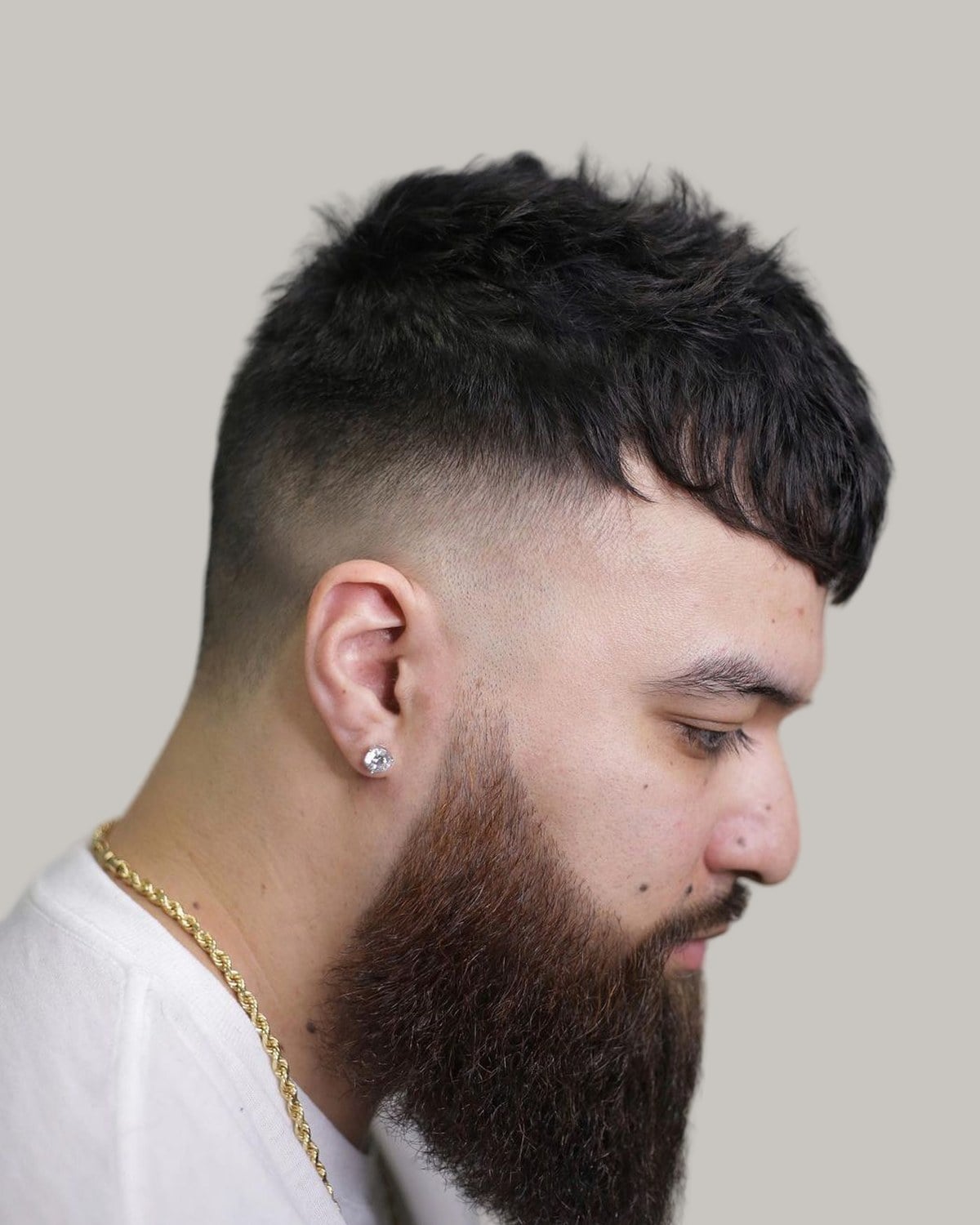 Man with a full beard and a fluffy Edgar haircut, a choppy fringe over a skin fade, seen in profile