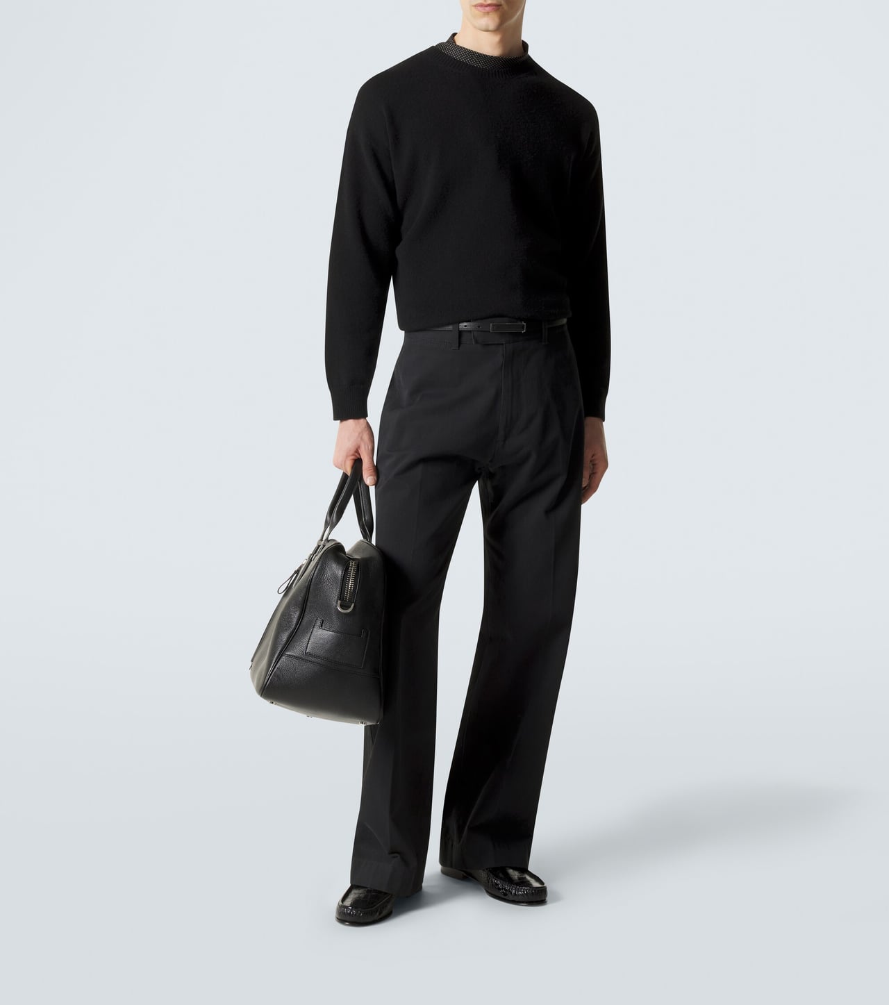 man in a black cashmere crewneck sweater with black trousers and black shoes, carrying a leather bag