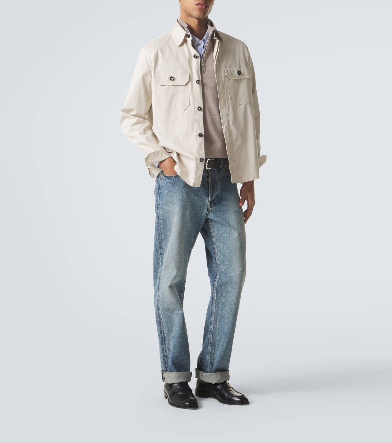 man in a beige cotton overshirt over a shirt with light blue jeans and black loafers