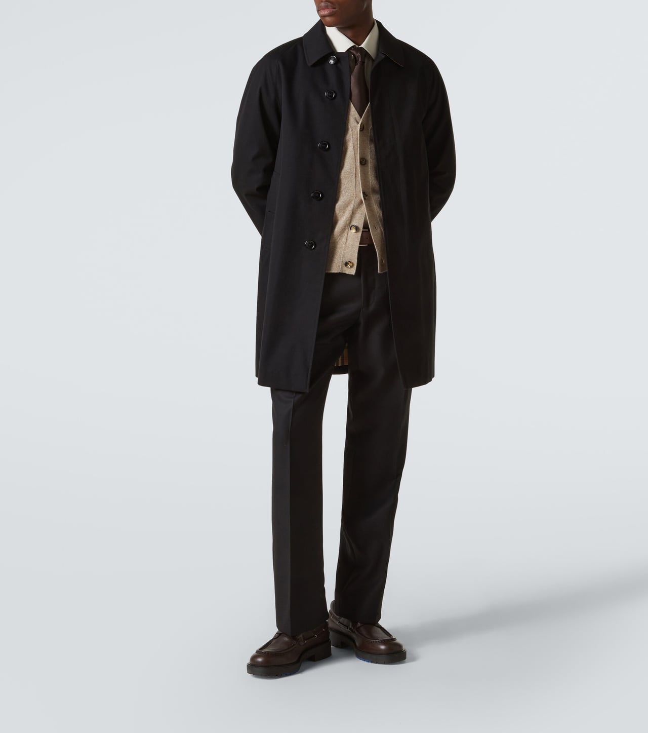 man in a black cotton gabardine car coat over a knit with dark trousers and black shoes