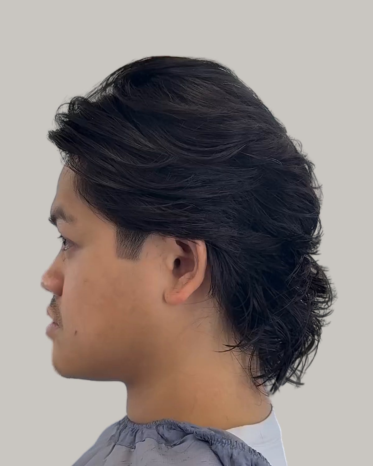 Man with a shaggy black wolf cut, seen in profile from the other side
