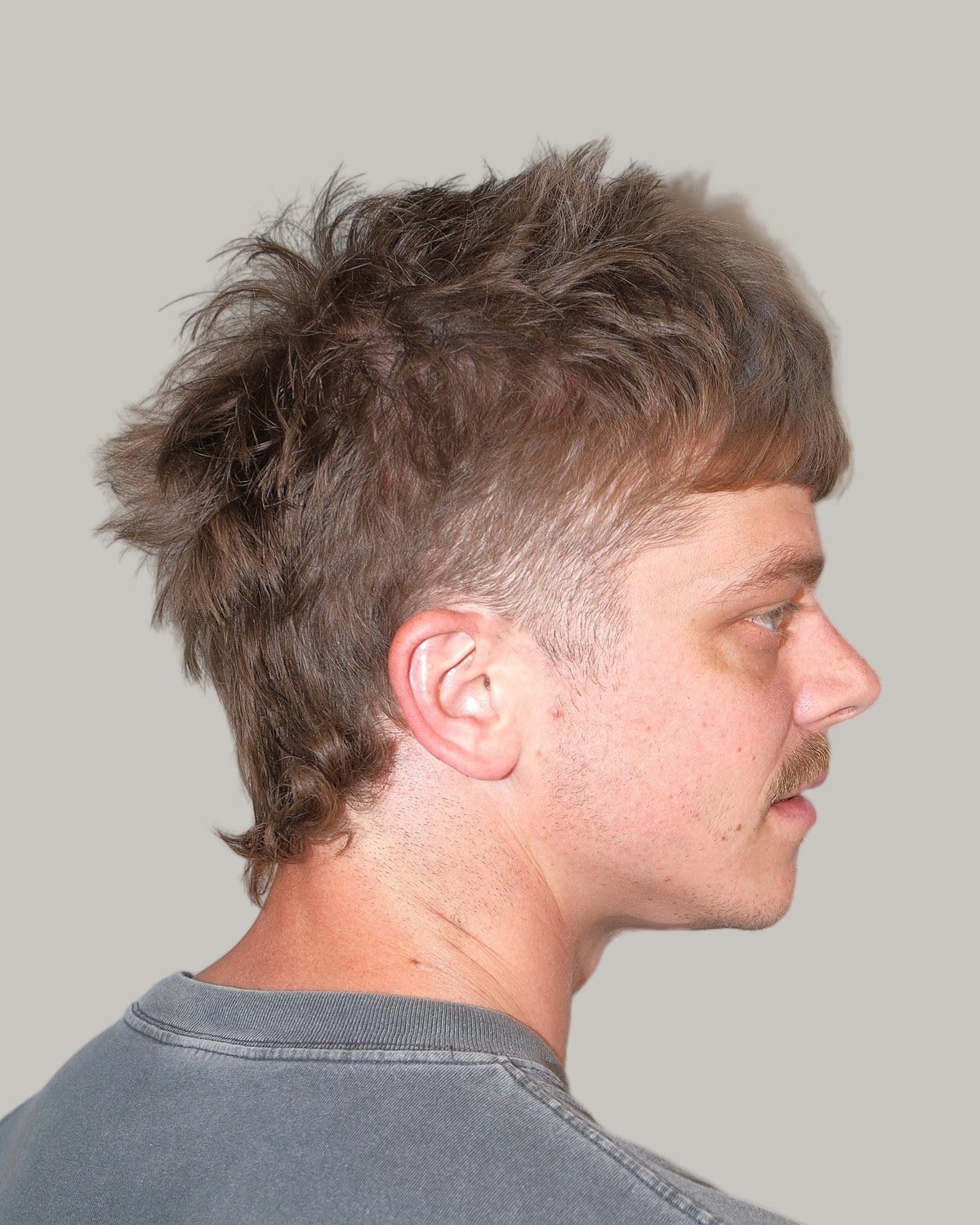 Man with a short, shaggy wolf cut and a mustache, seen in profile