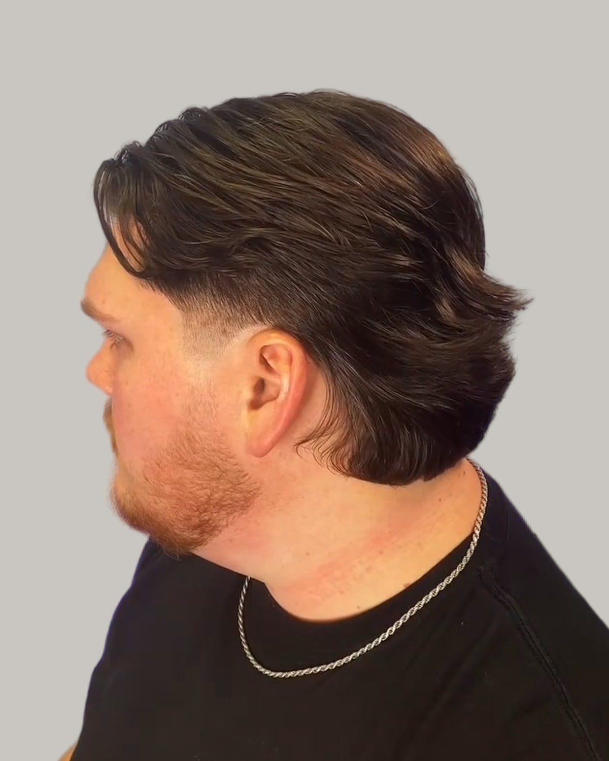 Bearded man with a tapered wolf cut combed back, seen in profile