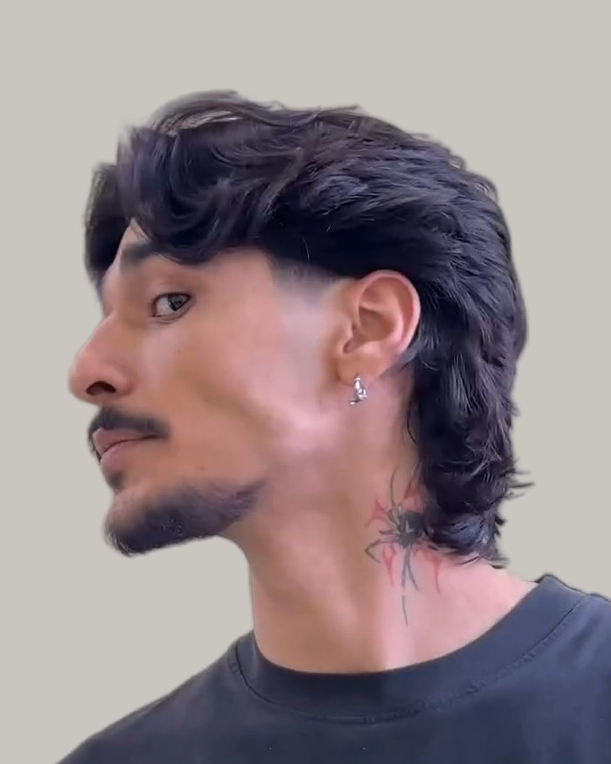 Man with a wavy wolf cut and a mustache, seen from the side at a three-quarter angle