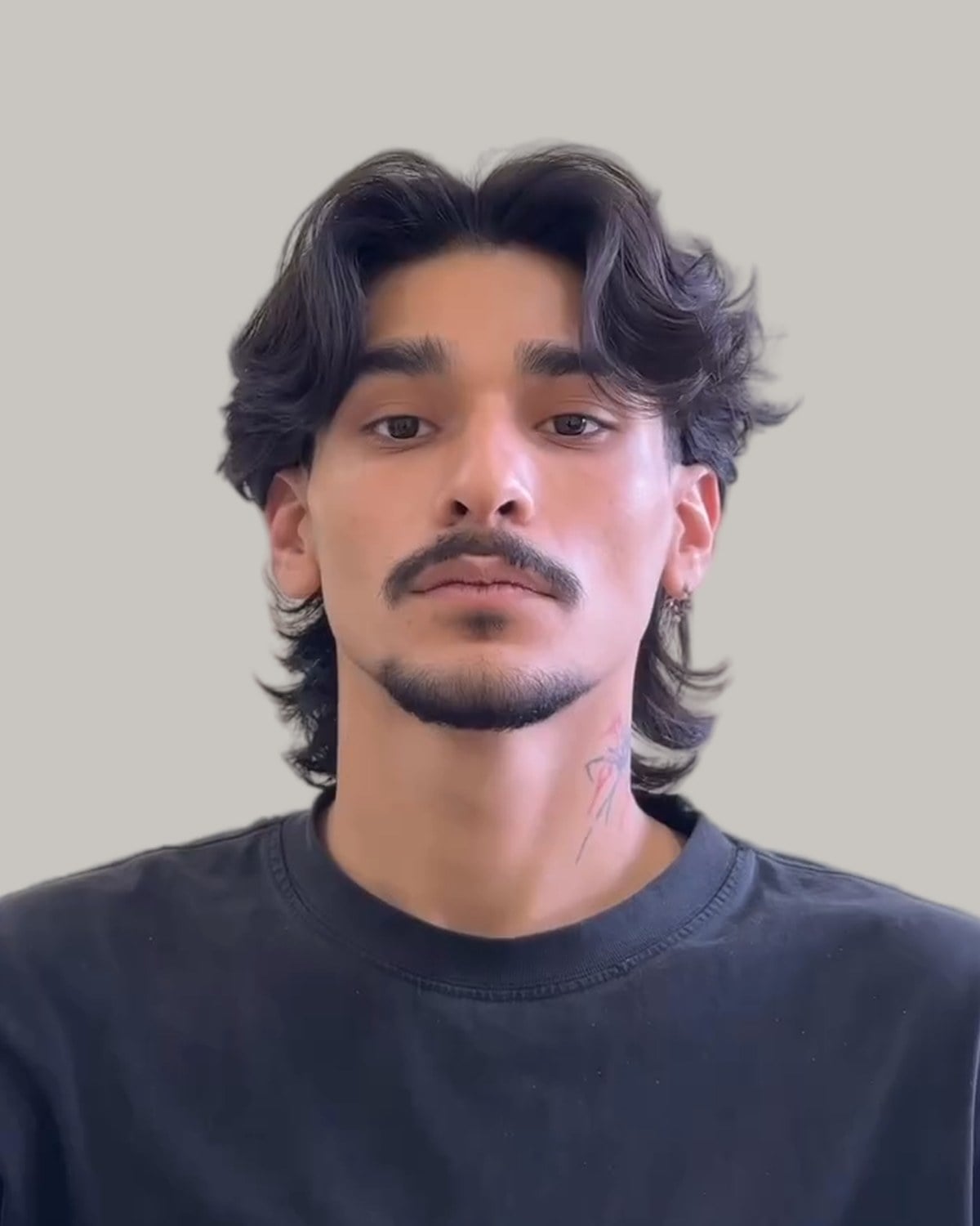 Man with a wavy wolf cut, a center part and a mustache, seen from the front