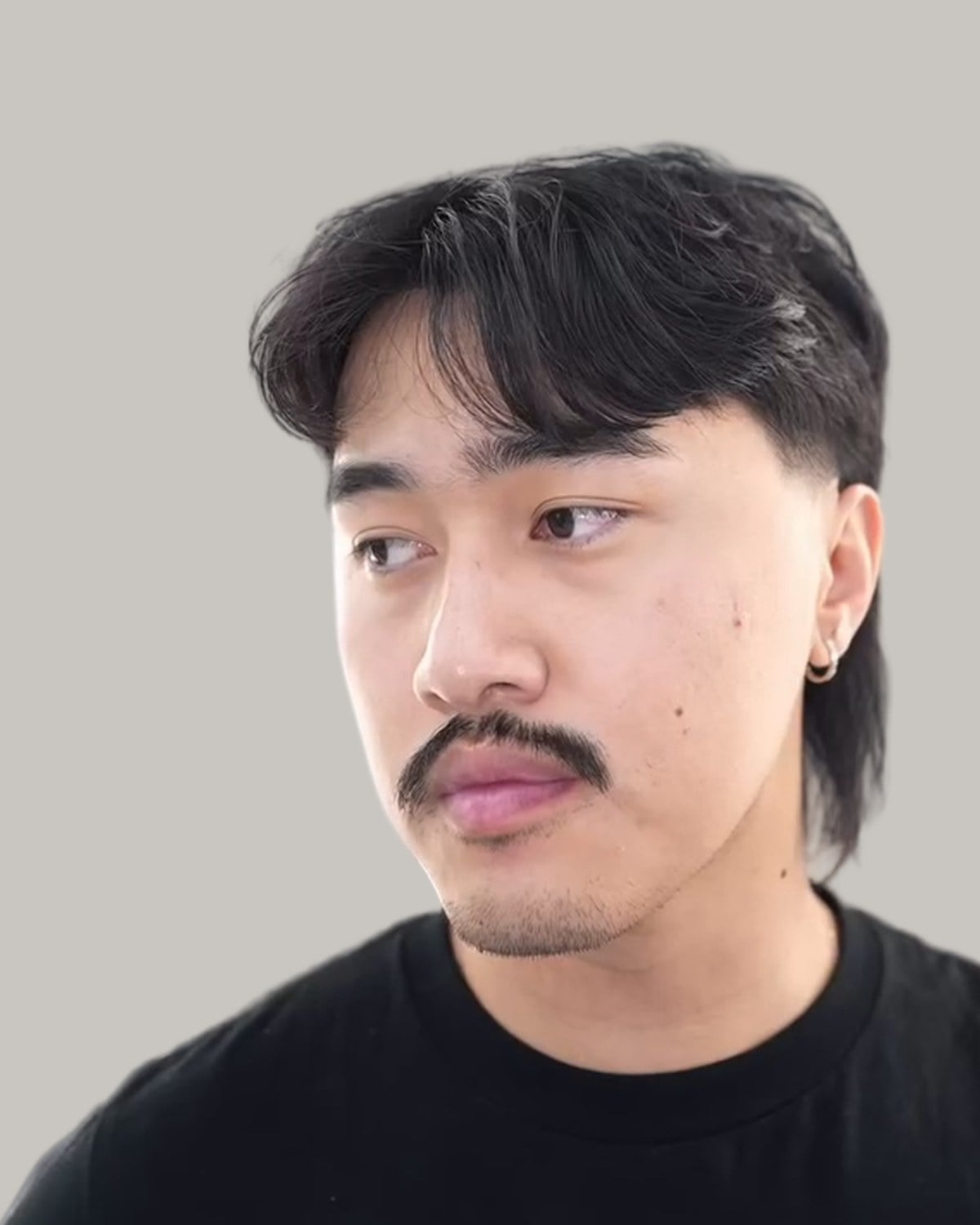 Man with a wolf cut, a choppy fringe and a mustache, seen from the front