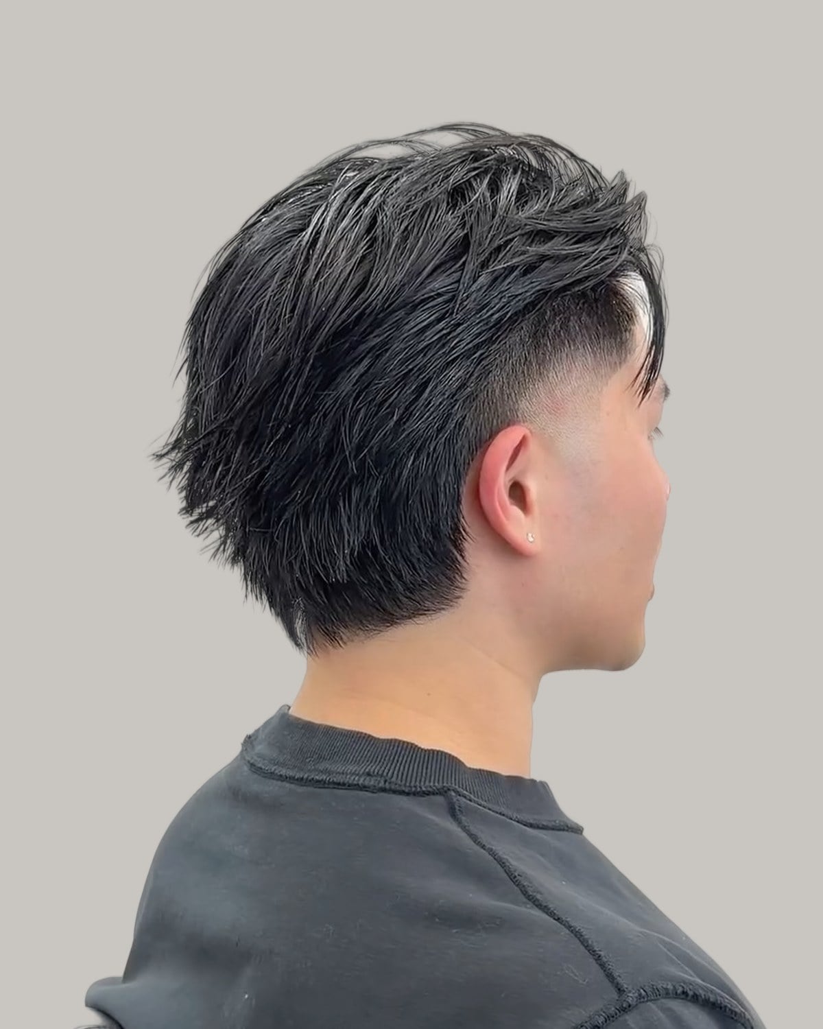 Man with a straight black mullet and a fringe, seen from behind at an angle