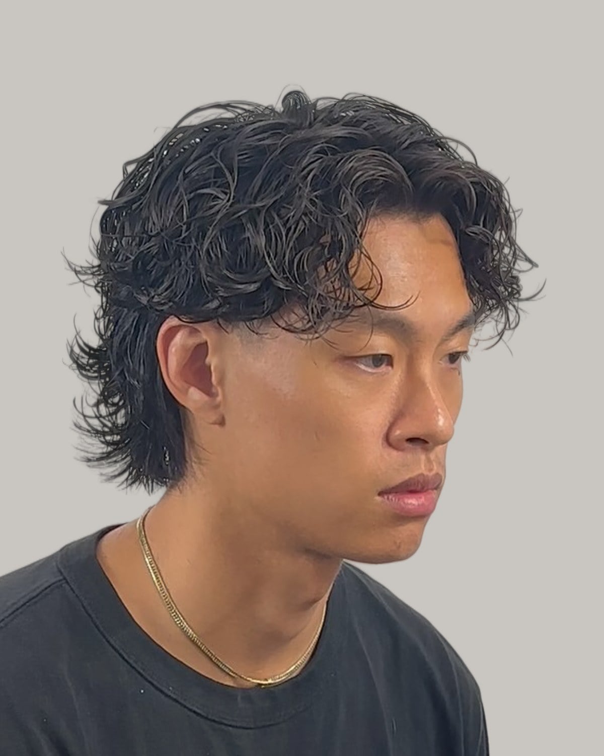 Man with a center-parted wavy black mullet, seen at an angle