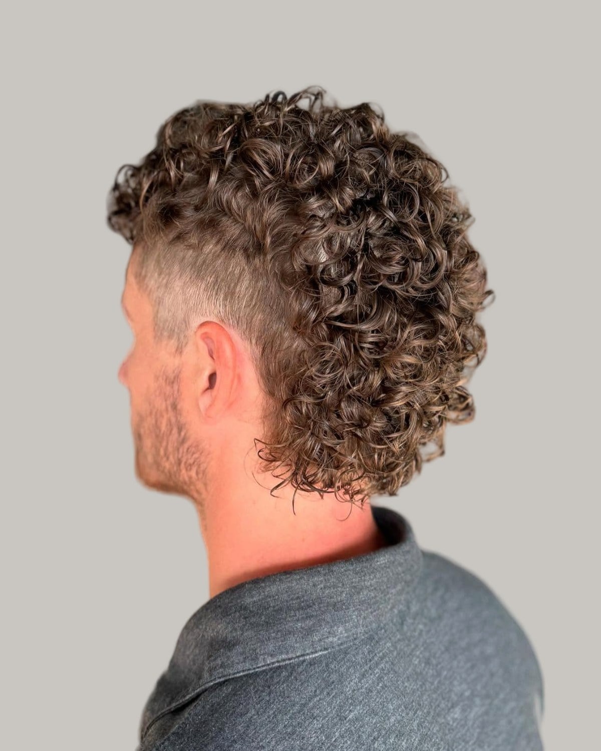 Man with a light brown curly mullet and a fade around the ear, seen from behind at an angle