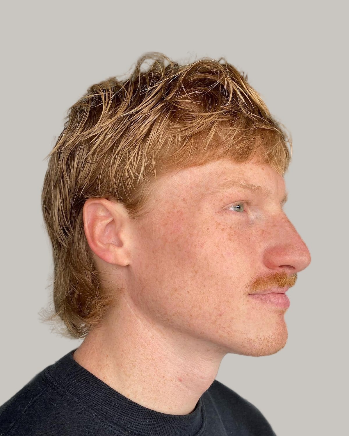Man with a ginger mullet and a mustache, seen at an angle