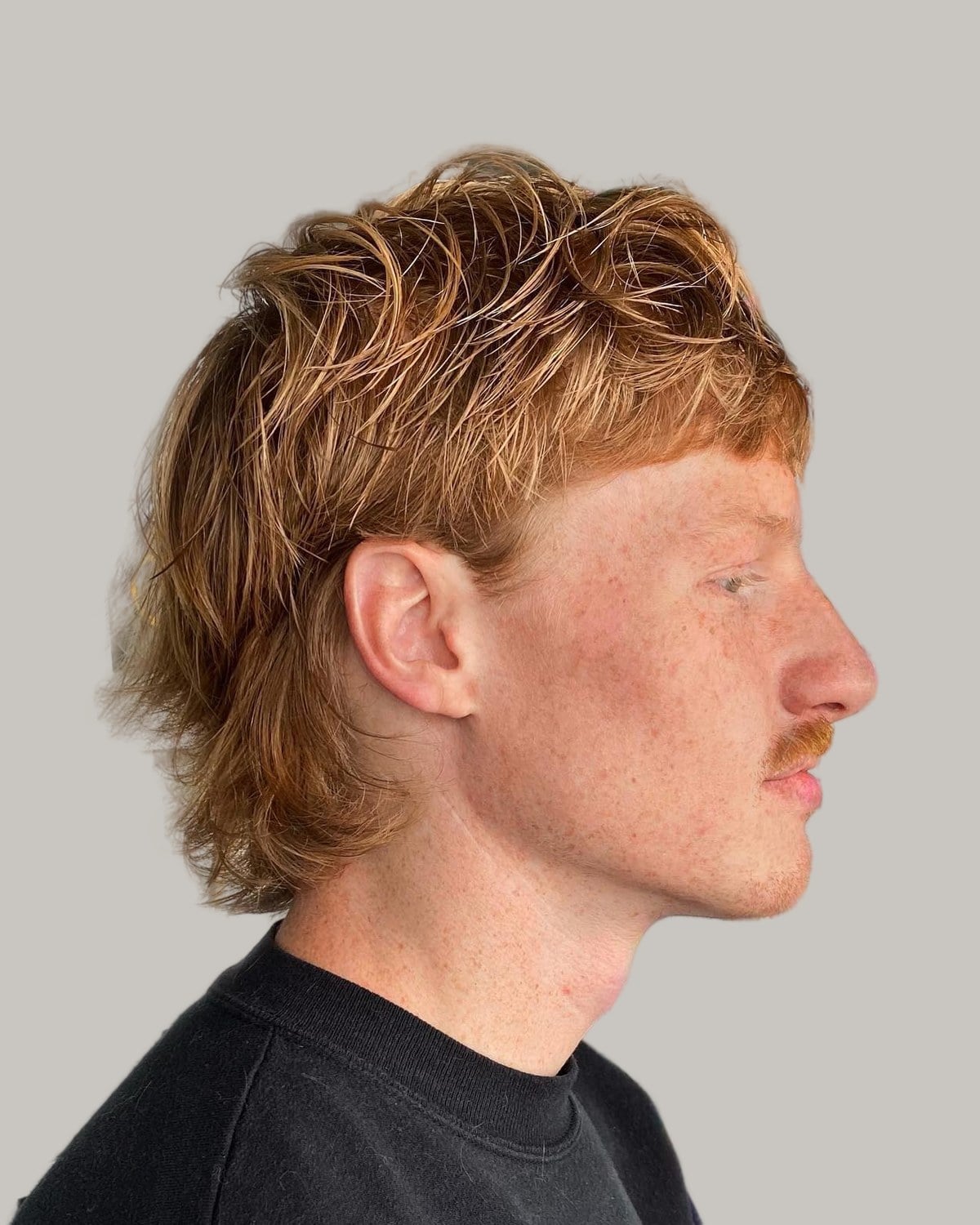 Man with a ginger mullet and a mustache, seen in profile