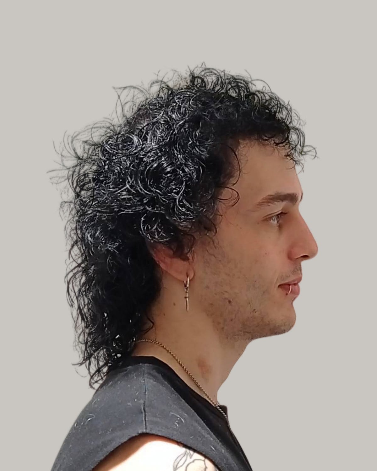 Man with long black curly hair cut into a mullet with short sides, seen in profile