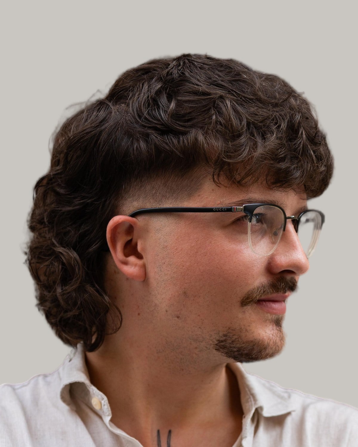 Man with glasses, a mustache and a brown curly mullet with a fade, seen at an angle