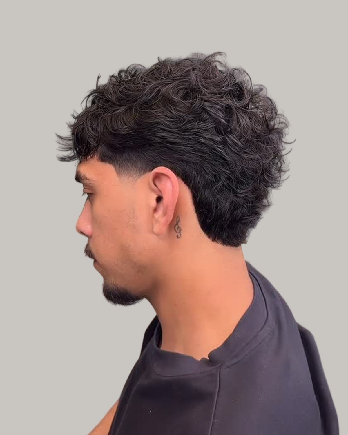Man with a dark curly mullet and a low fade, seen in profile