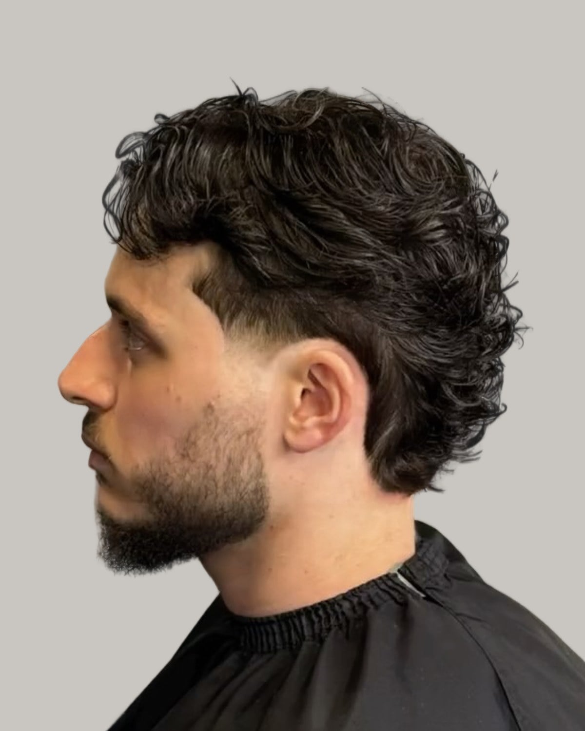 Bearded man with a dark curly mullet, seen in profile