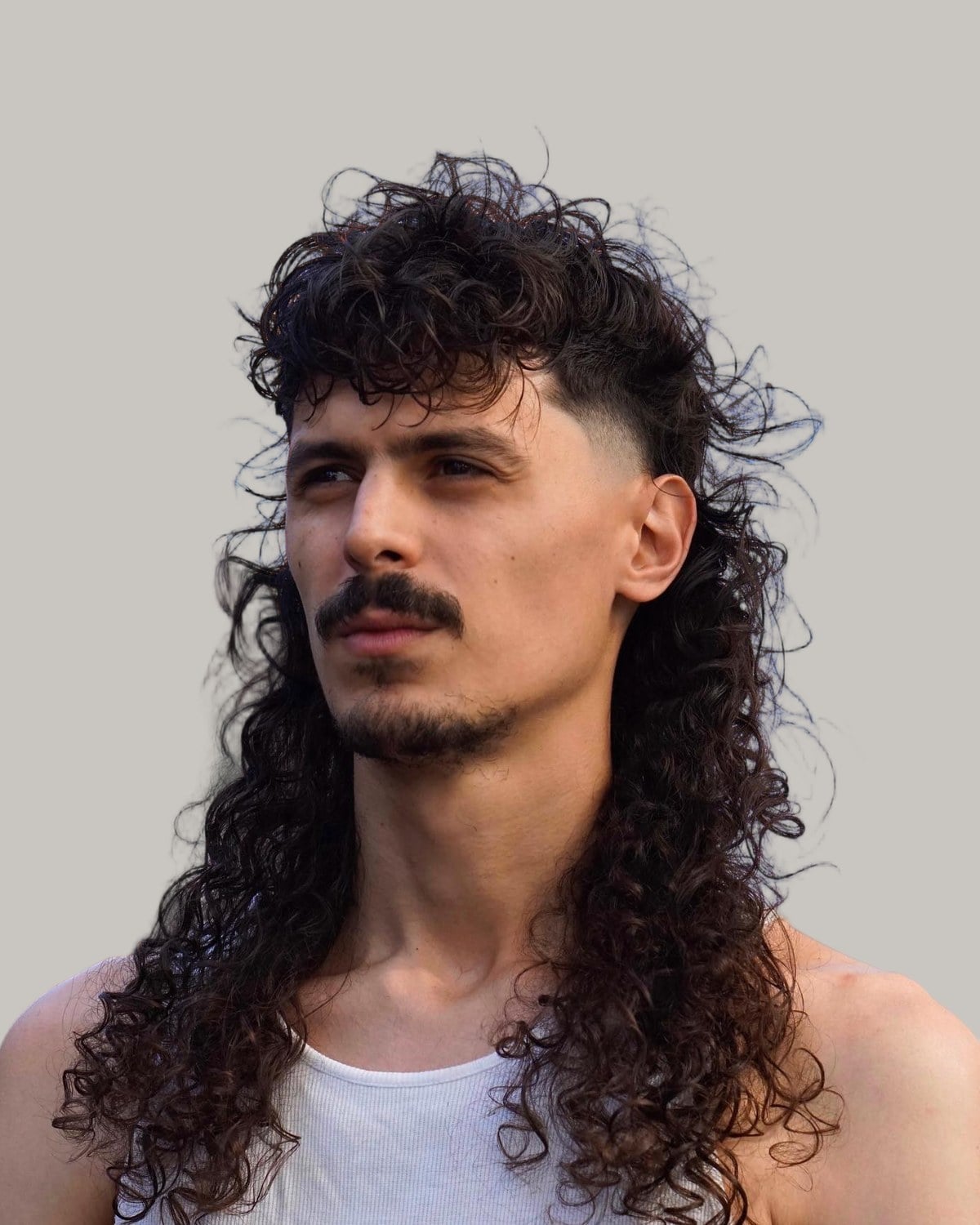 Man with a mustache and a long black curly mullet with faded sides, seen at an angle