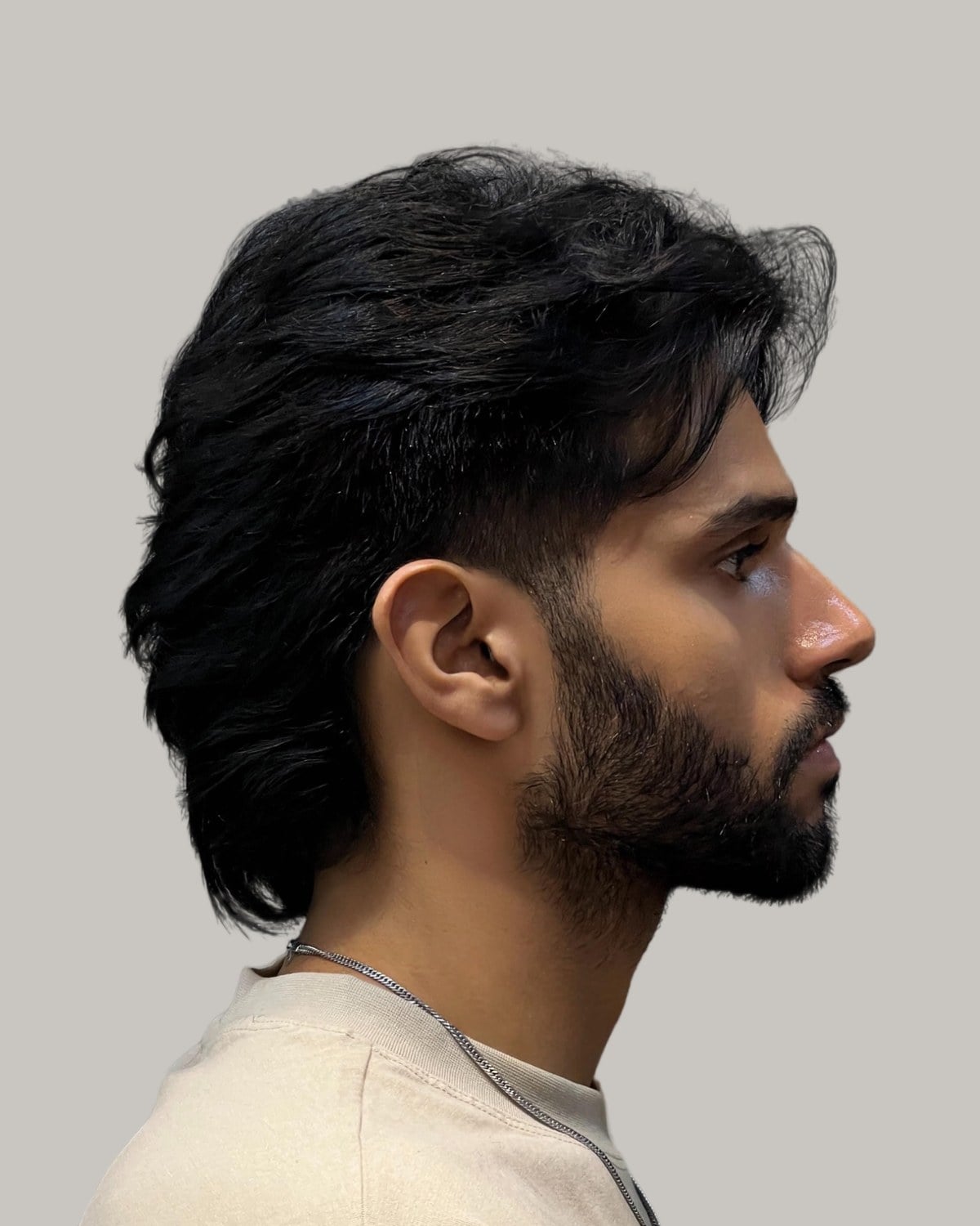 Bearded man with long black hair cut into a mullet, seen in profile