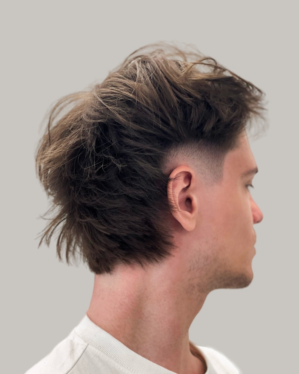Man with a messy brown mullet and a skin fade, seen in profile