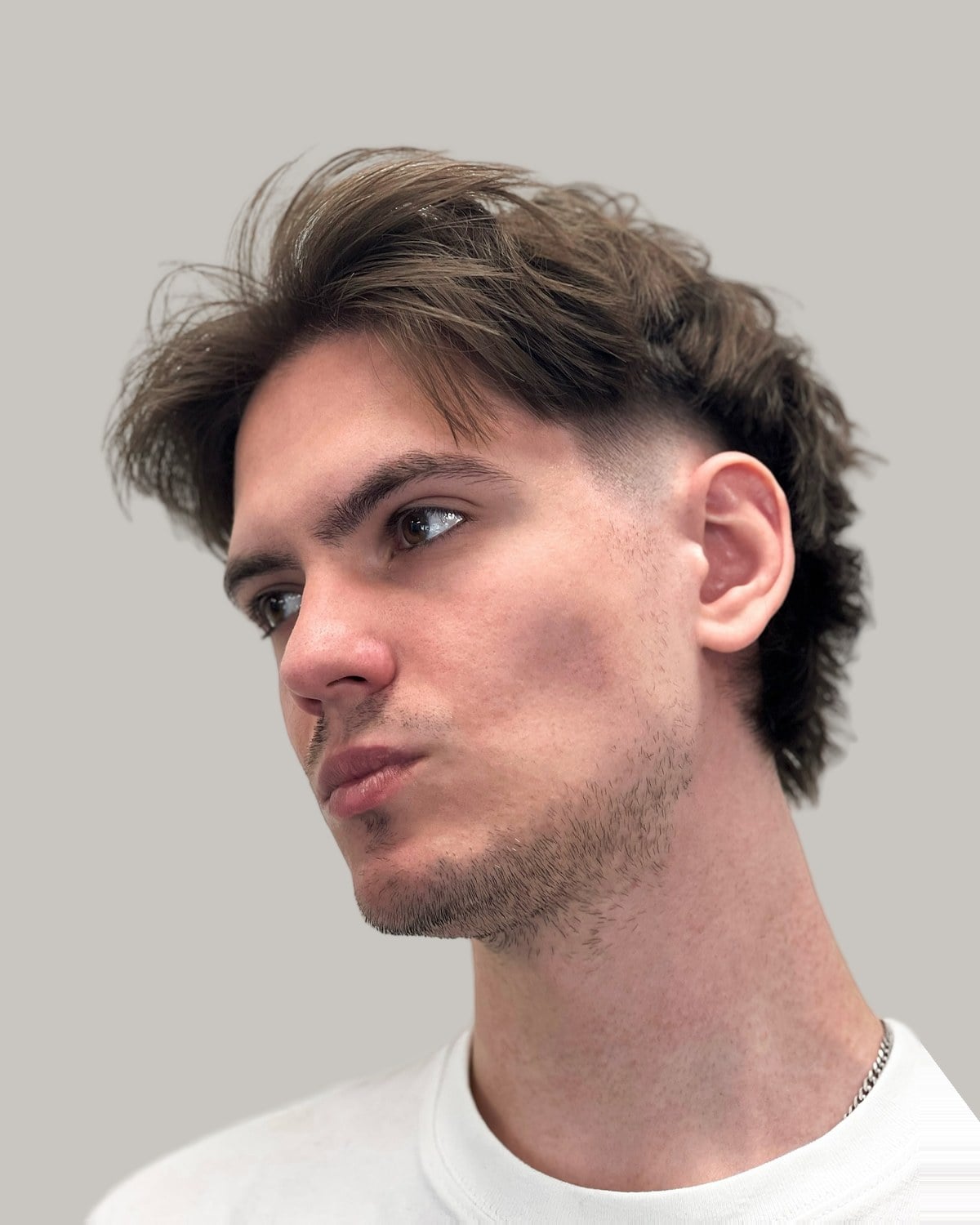 Man with a messy brown mullet and a skin fade, seen at an angle