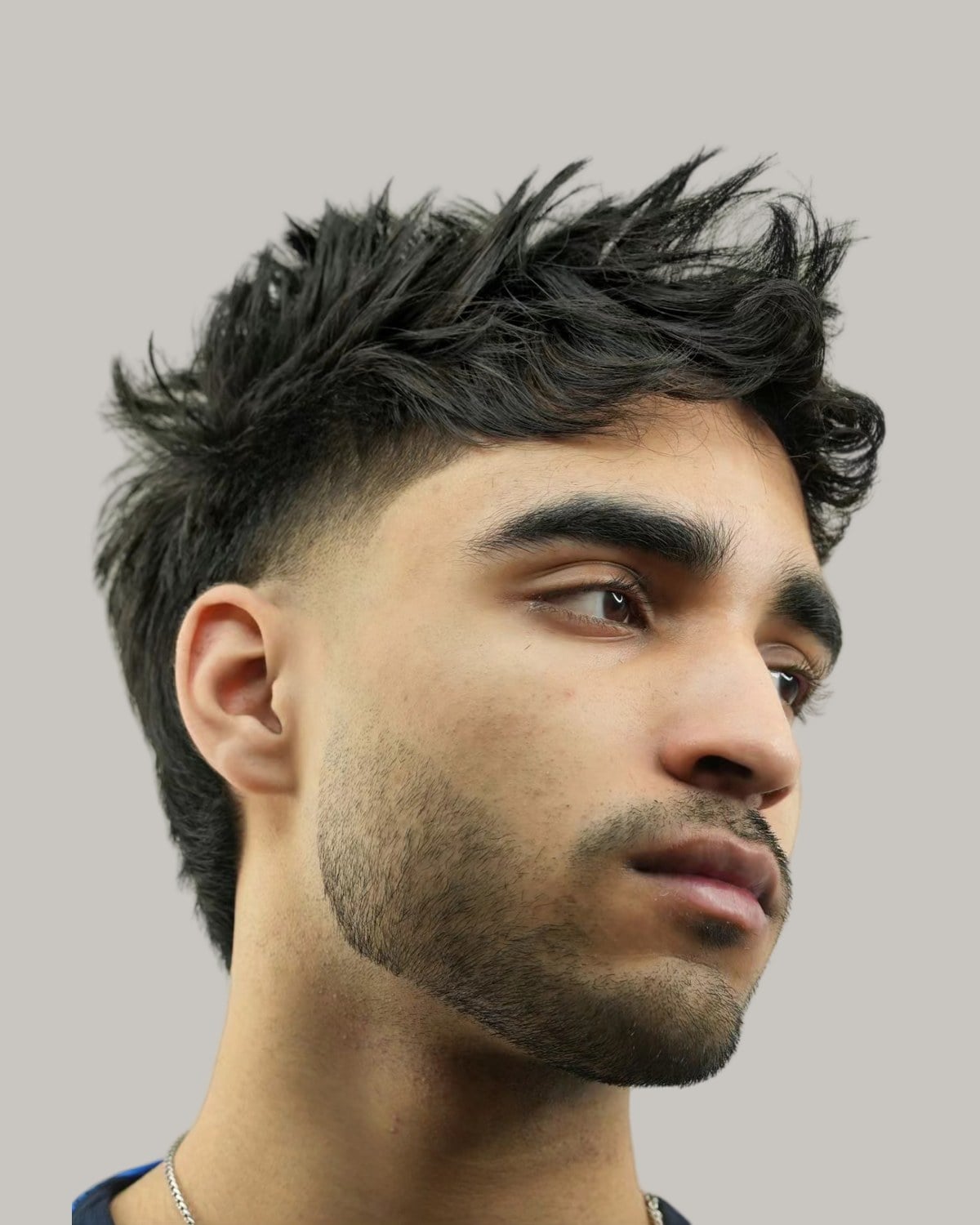 Man with a short beard and a spiky dark mullet with a mid taper, seen at an angle