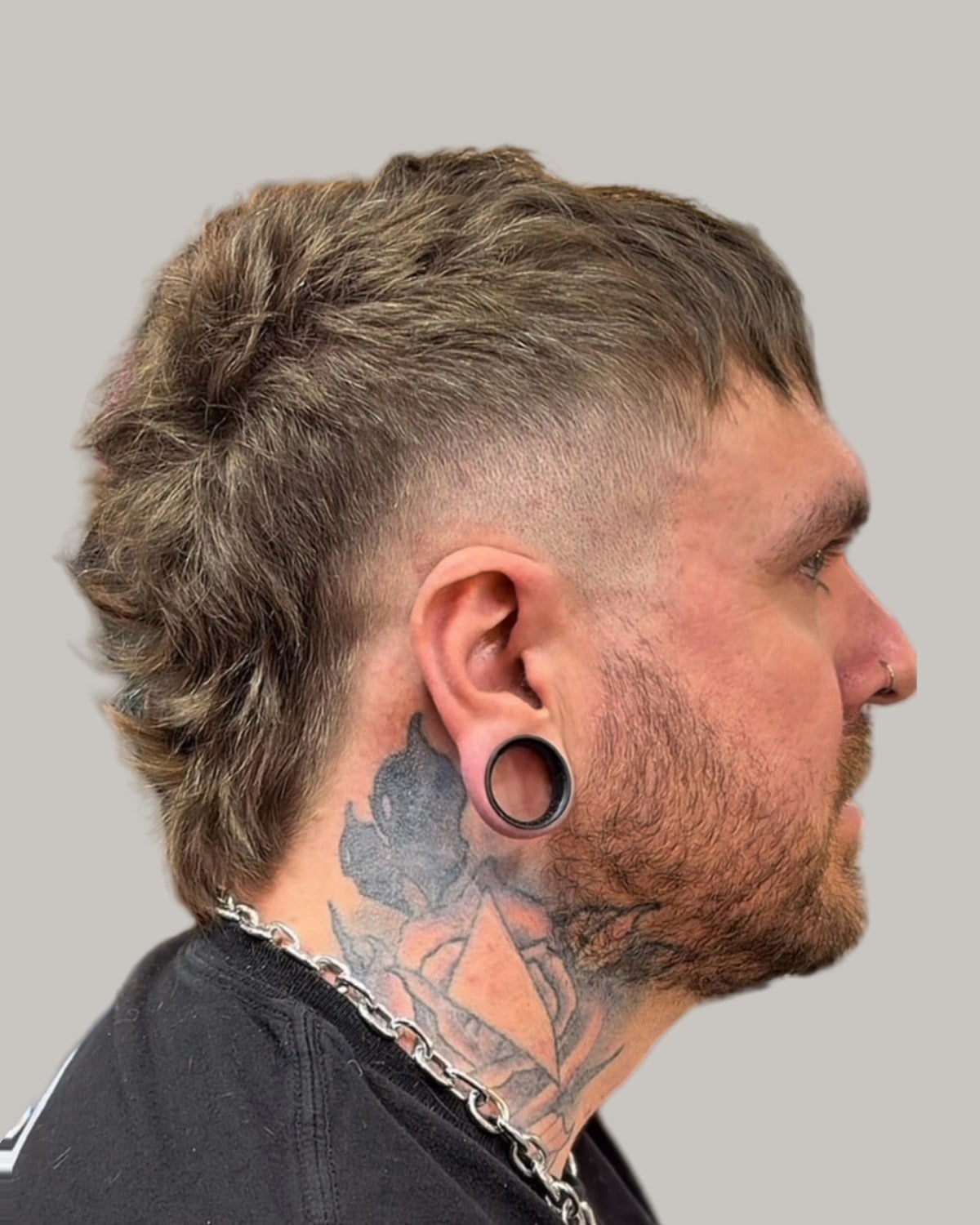 Man with a textured mohawk mullet, faded sides and ear gauges, seen in profile