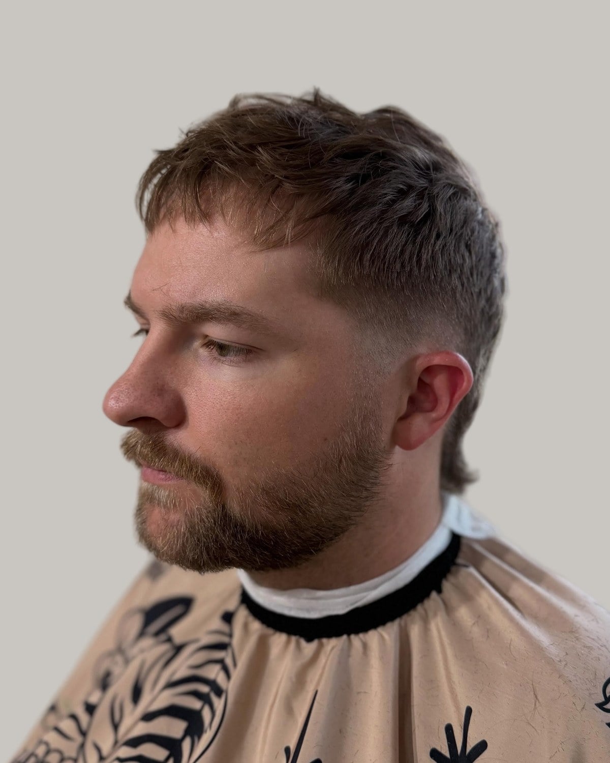 Bearded man with a short textured mullet and a mustache, seen at an angle